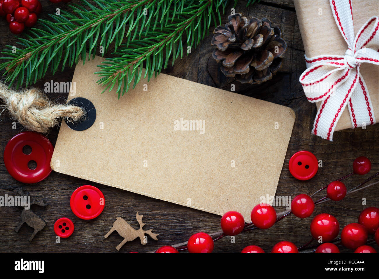 Christmas concept with an empty greeting card, fir branches, pine cone and a gift and red decorative buttons with wooden nordic reindeer on rustic woo Stock Photo
