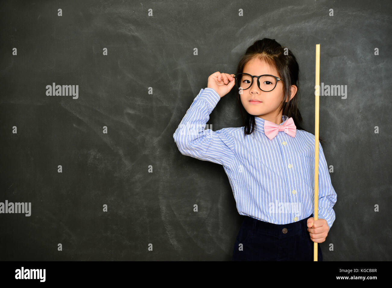young pretty female tutor using stick teaching study class and standing in chalk blackboard background. school education concept. Stock Photo