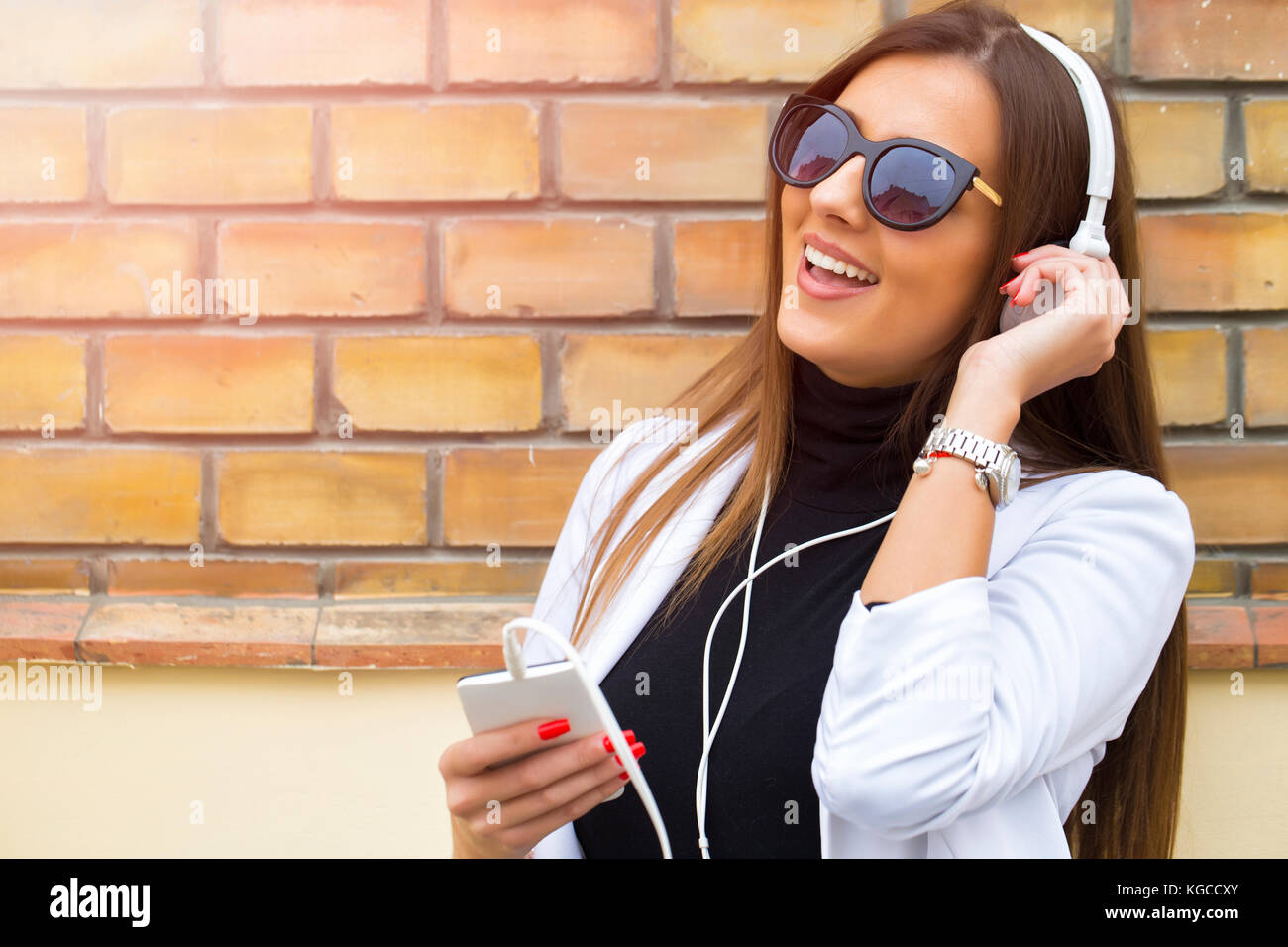 Happy young woman with sunglasses listening to music via headphones on ...