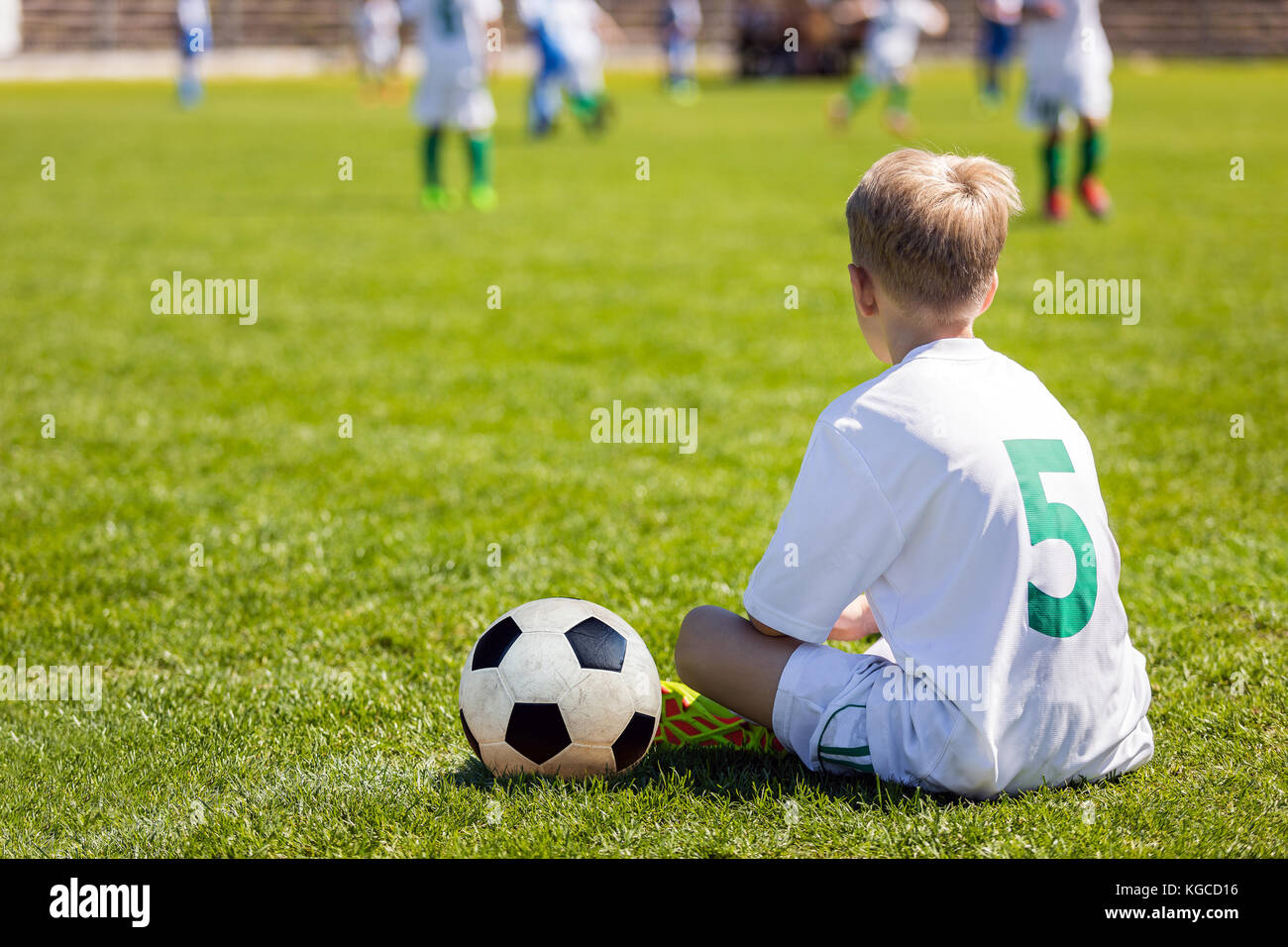 Young Boy as a Soccer Player. Kid Sitting on Football Pitch. Soccer