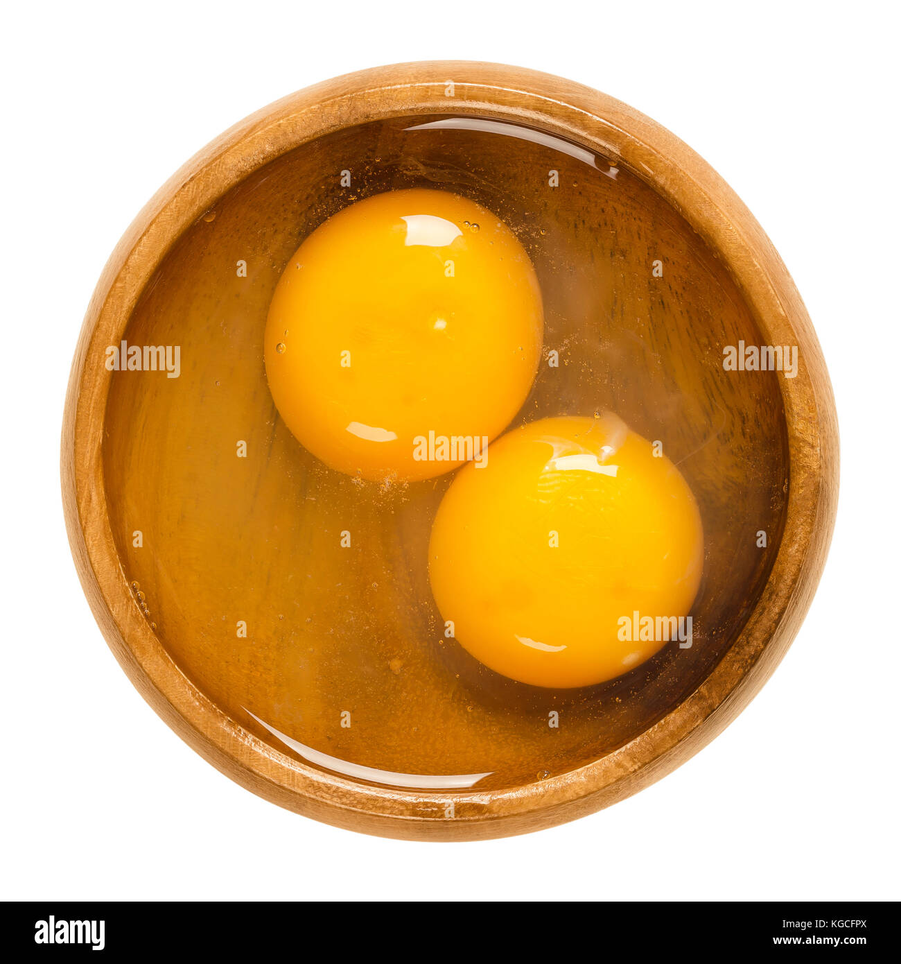 Two raw chicken eggs cracked into a wooden bowl. Yolk and white without eggshells. Common food and versatile ingredient in cooking. Photo. Stock Photo