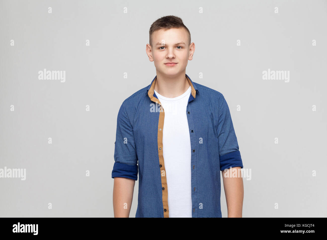 Young  boy wearing blue shirt looking at camera and smile. Studio shot, gray background Stock Photo