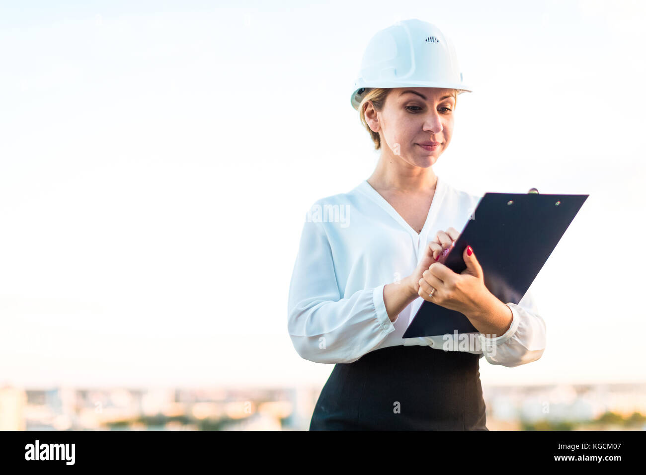 Pretty young forewoman in helmet stand on the roof with tablet i Stock Photo