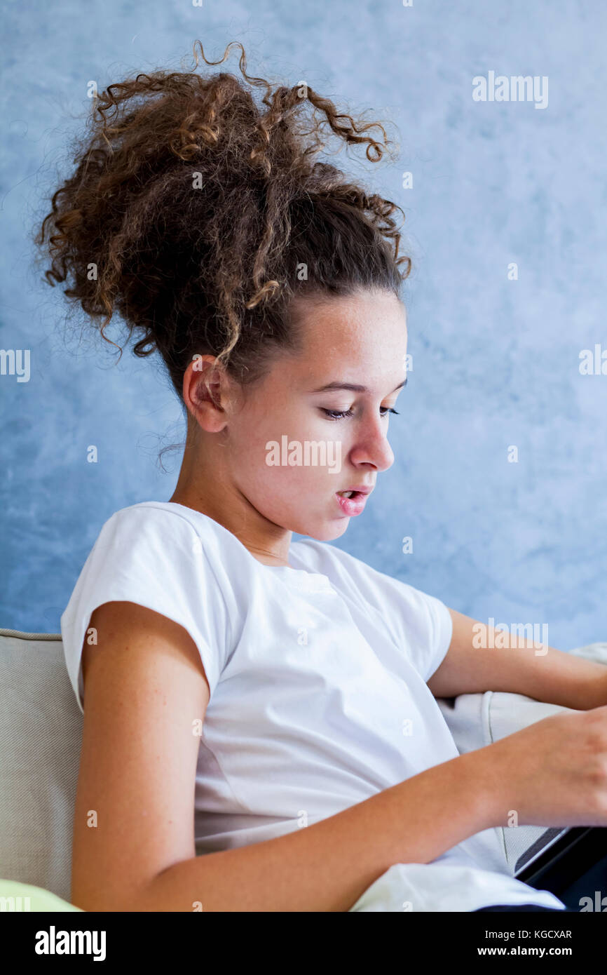 Side view at curly hair girl using digital tablet on sofa Stock Photo