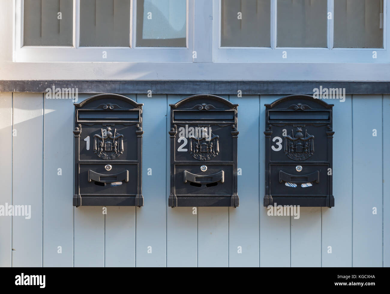 Three black external letter boxes numbered 1 to 3 mounted on pale wood panel underneath a window Stock Photo