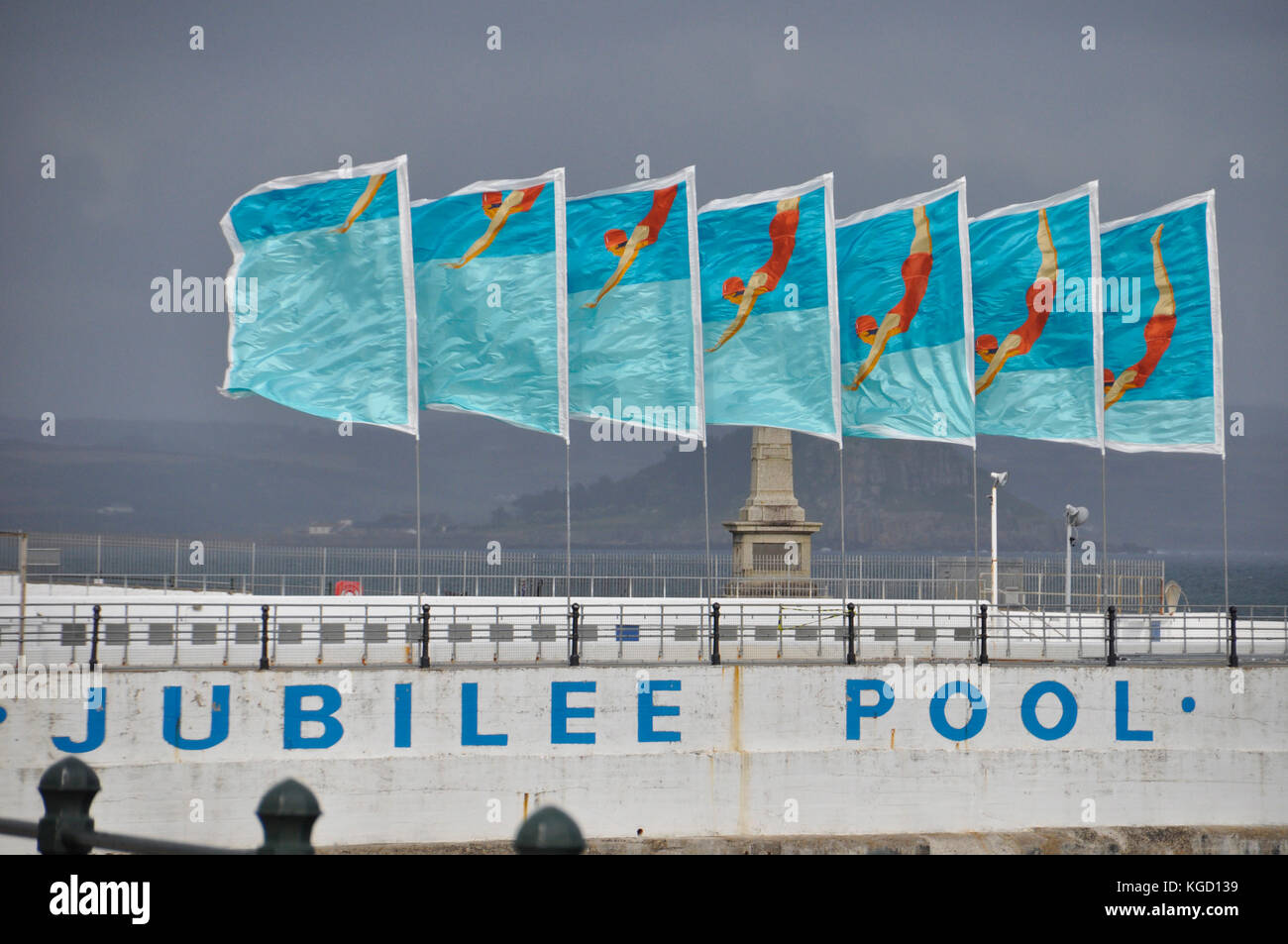 Bright coloured flags flutter in a strong sea breeze on the Jubilee swimming pool in Penzance. Cornwall.UK Stock Photo