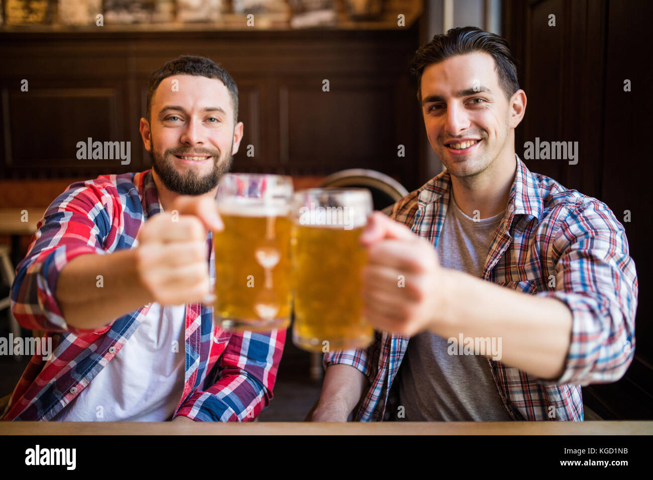 Having a pint with friend. Two cheerful young men in shirt toasting