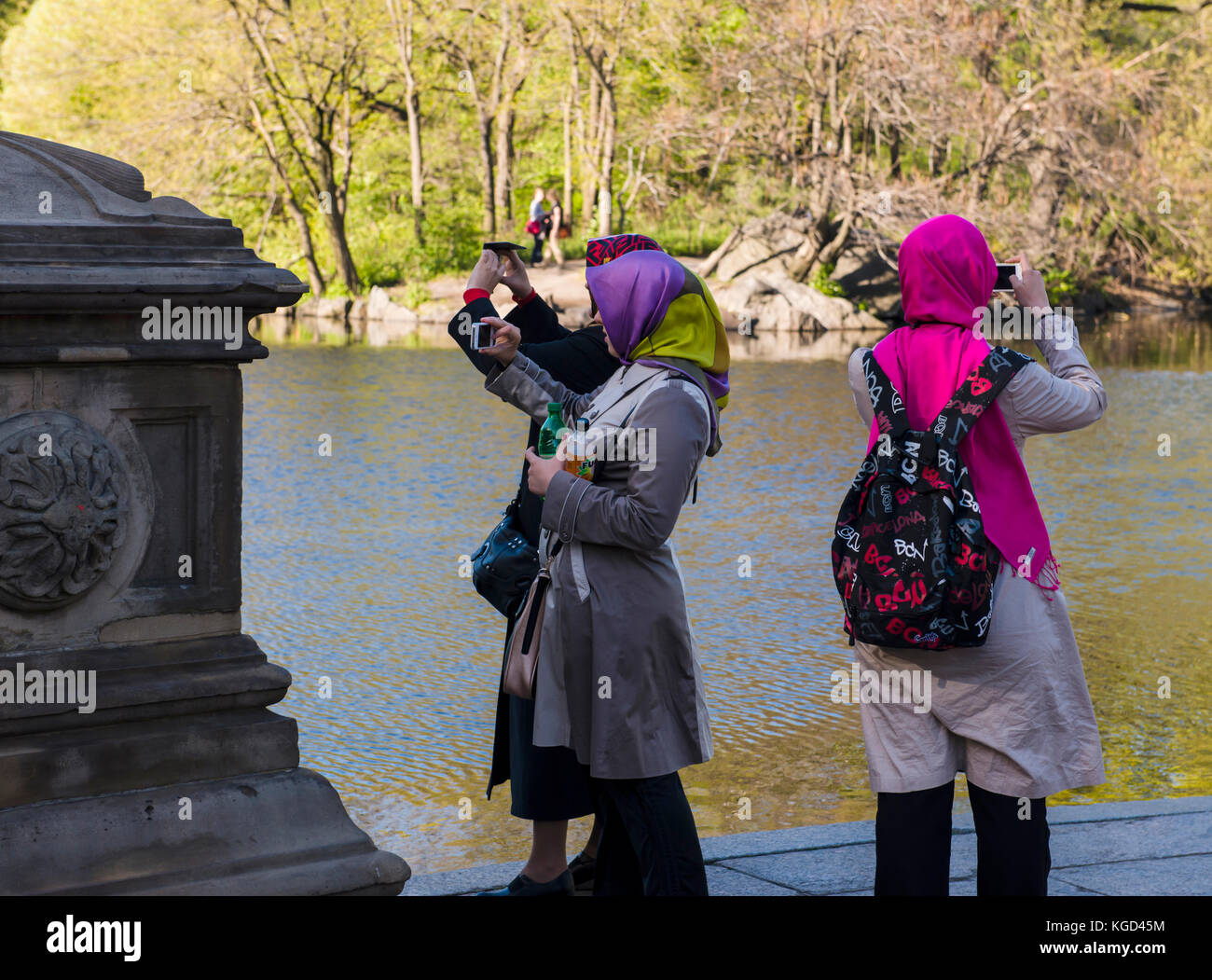 Three ladies wearing headscarves take pictures of a pond. Stock Photo