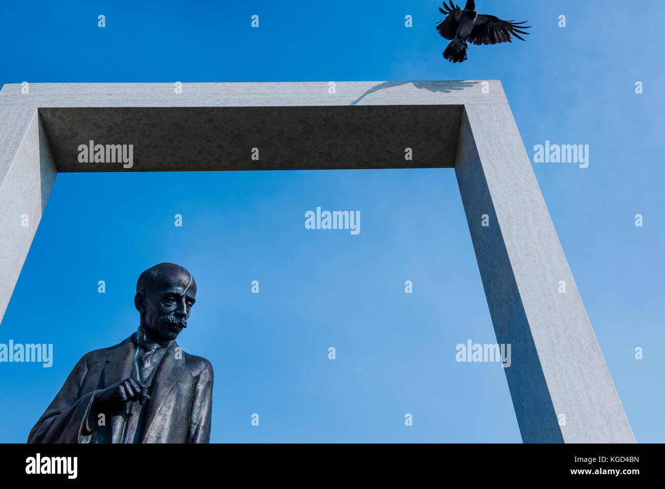 Statue with pensive expression against the blue sky while black bird takes off above the sculpture. Stock Photo