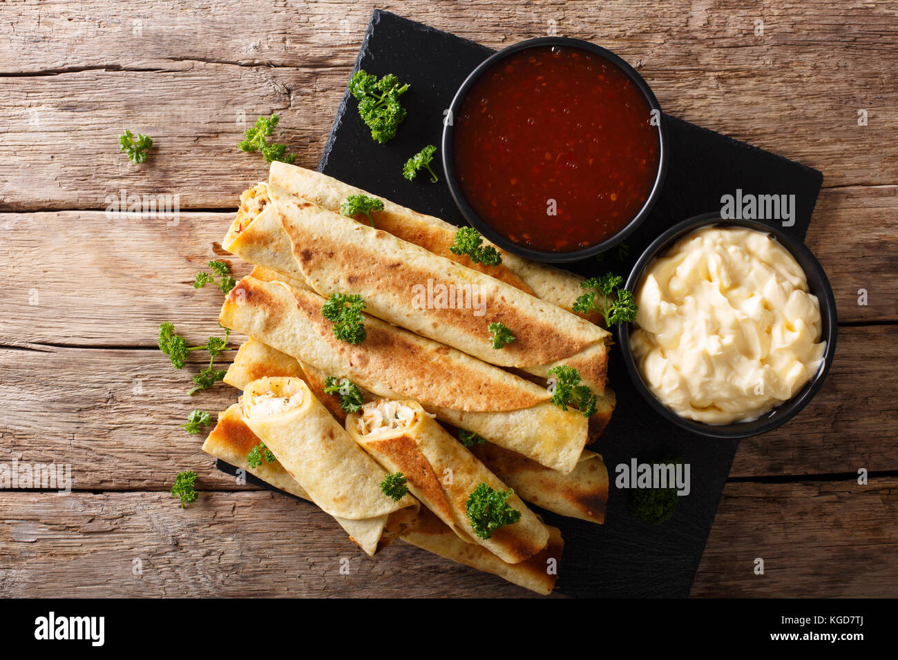 Mexican taquitos with chicken and cheese stuffing close-up, and sauces on the table. horizontal top view from above Stock Photo
