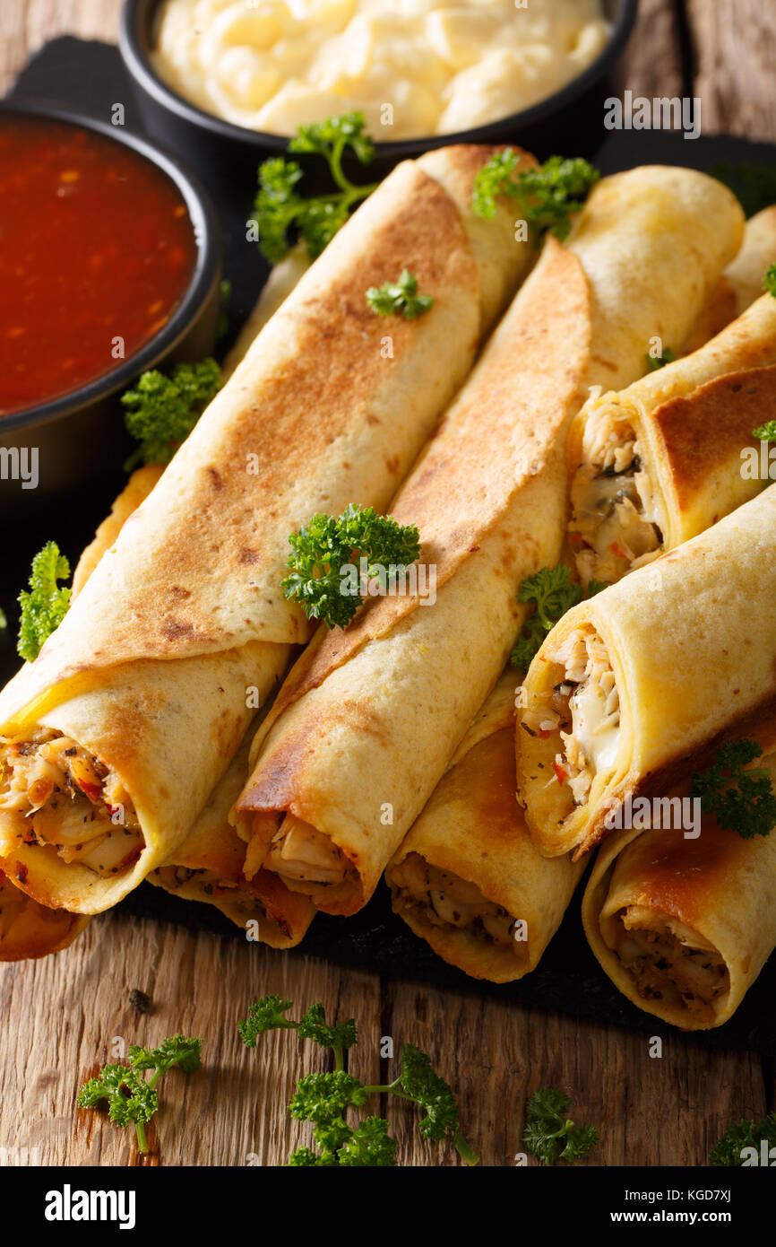 Mexican taquitos with chicken and cheese stuffing close-up, and sauces on the table. vertical Stock Photo