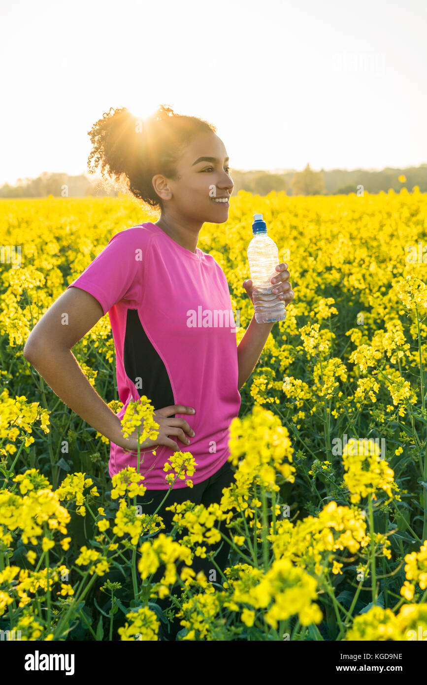 Outdoor portrait of beautiful happy mixed race African American girl teenager female young woman athlete runner drinking water from a bottle in a fiel Stock Photo