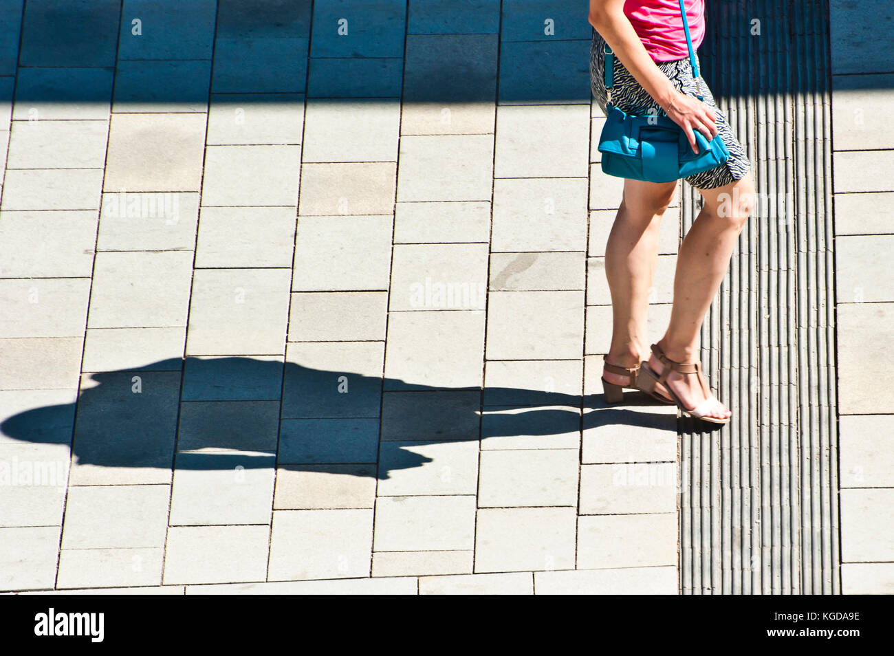 woman  in skirt walking along a street in summer, projecting shadow on the pavement Stock Photo