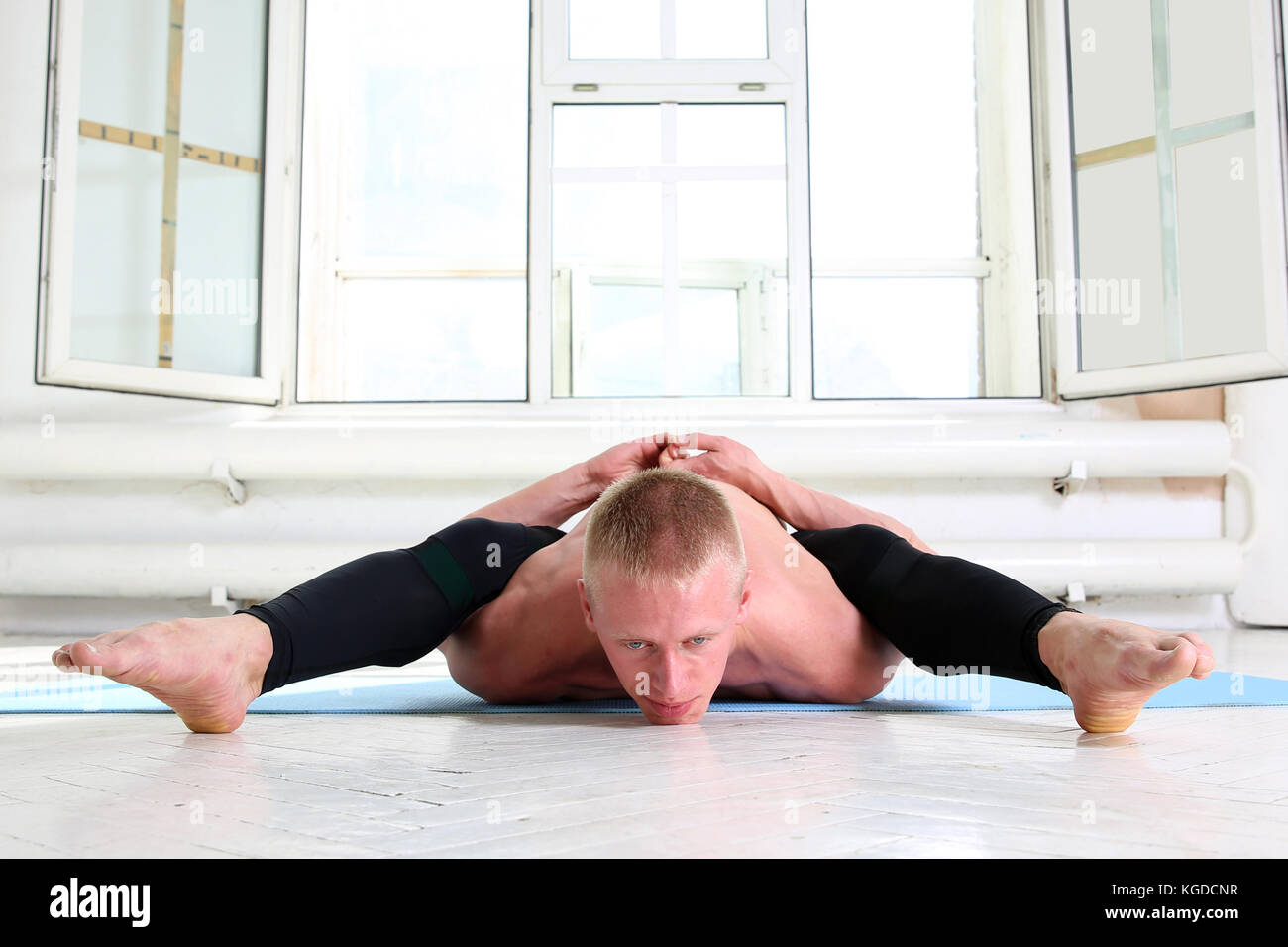 Beautiful sporty man practicing yoga. Asana Kurmasana. Tortoise pose. Tortoise posture Stock Photo