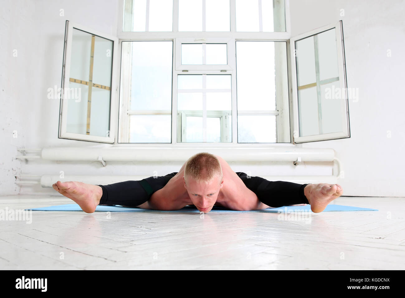 Beautiful sporty man practicing yoga. Asana Kurmasana. Tortoise pose. Tortoise posture Stock Photo
