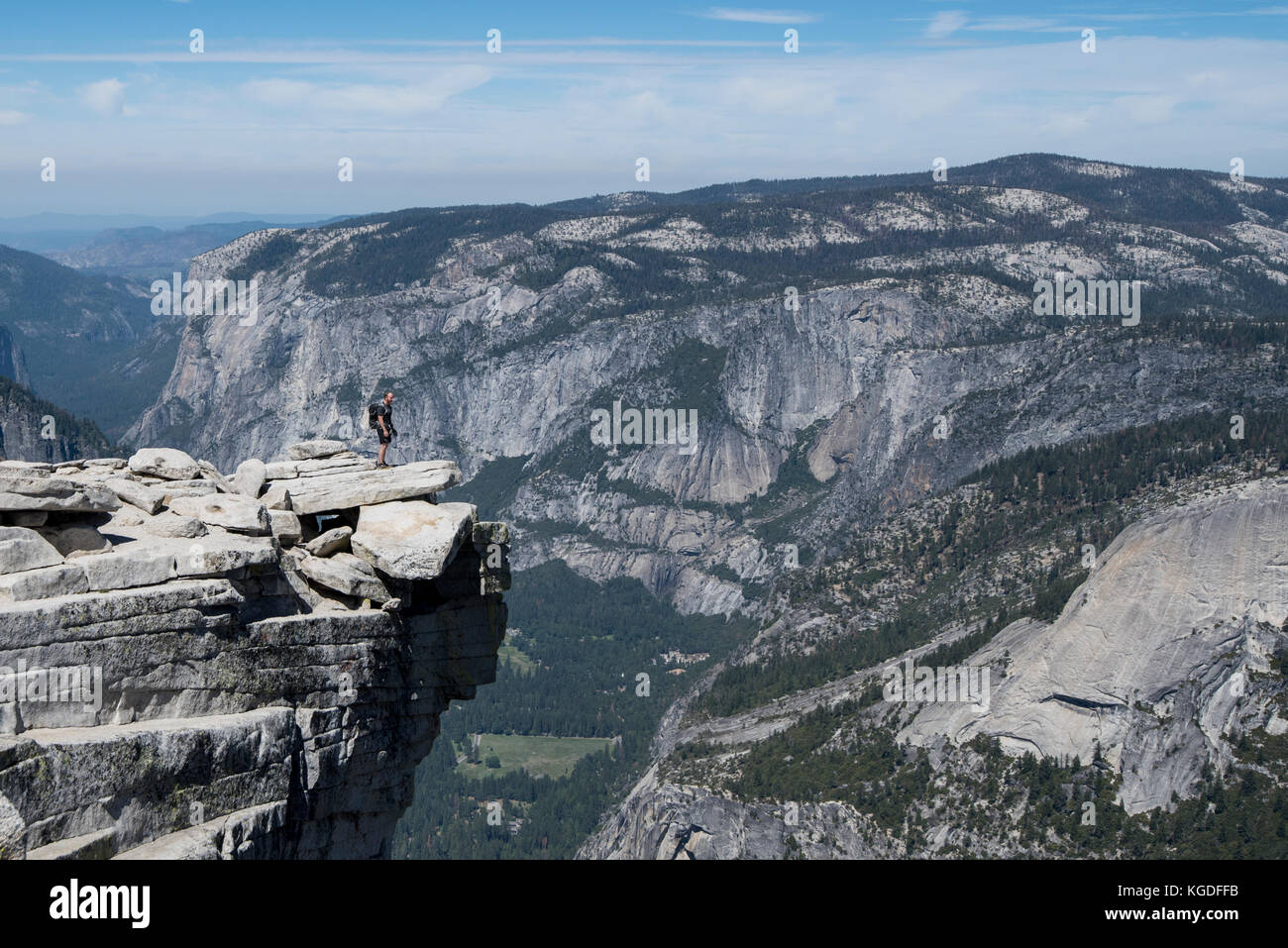 A man stands triumphantly on top of Half Dome with Yosemite Valley in the background in Yosemite National Park. Stock Photo