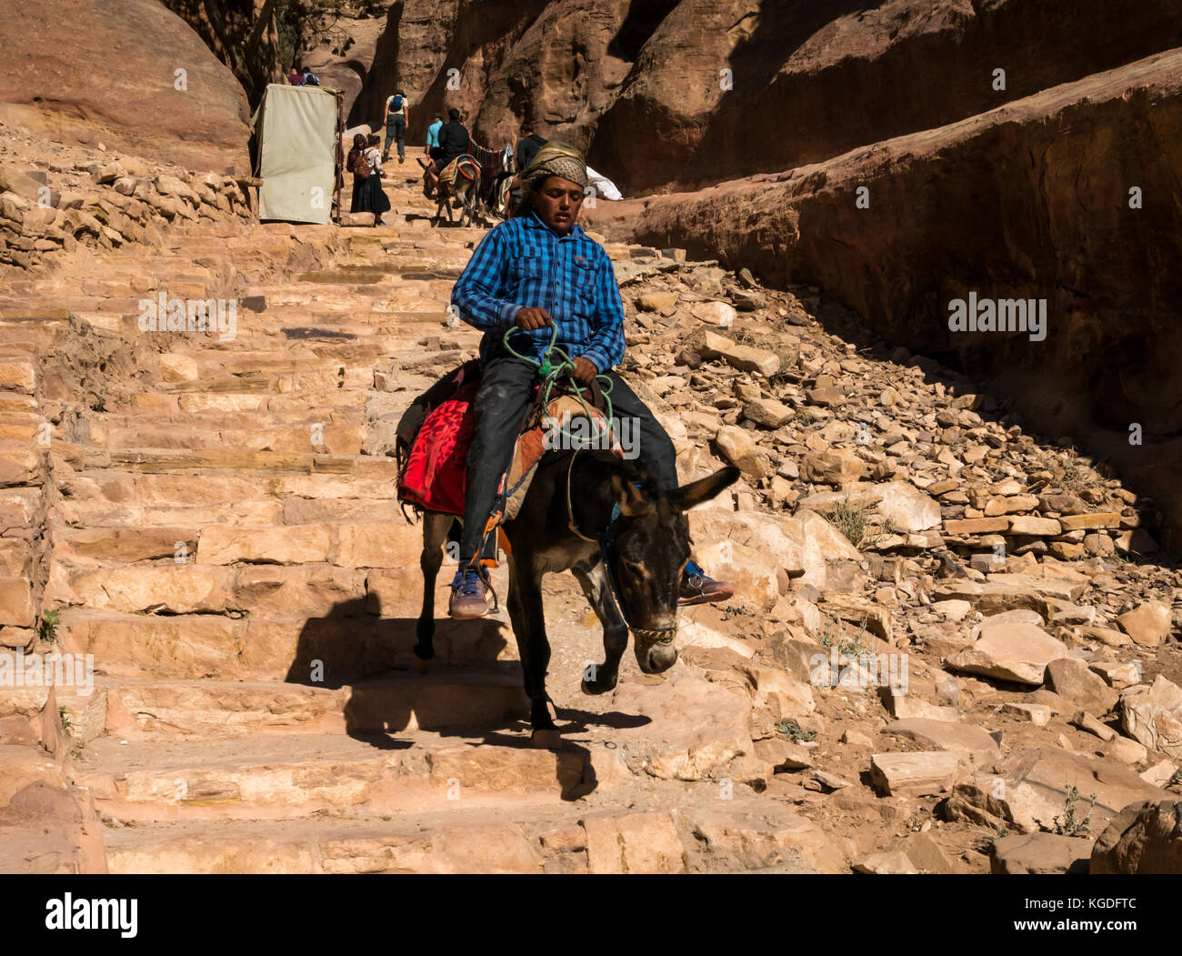 Local Bedouin boy riding donkey down carved sandstone steps of route to Ad Deir, the Monastery, Petra, Jordan, Middle East, to get a tourist fare Stock Photo