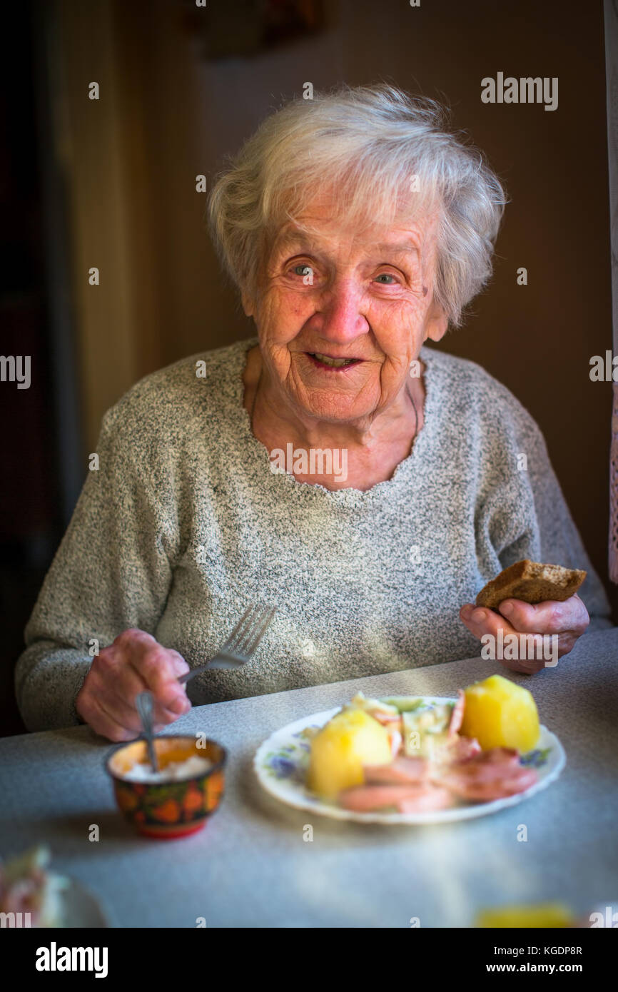 An elderly woman eating lunch sitting at the table. Stock Photo
