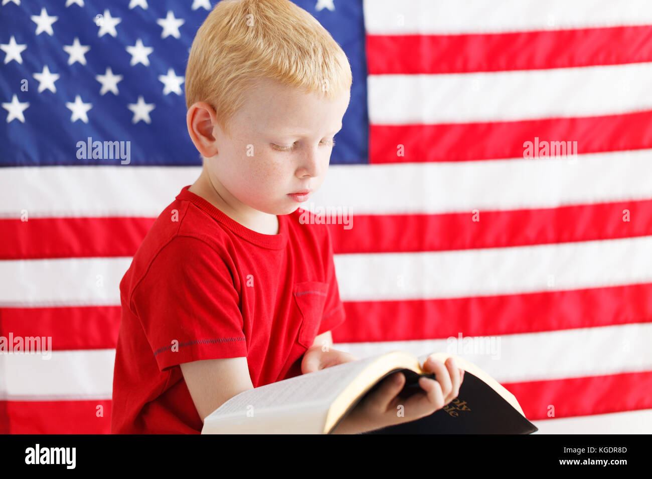 American little boy reading Holy Bible . American flag on a background Stock Photo