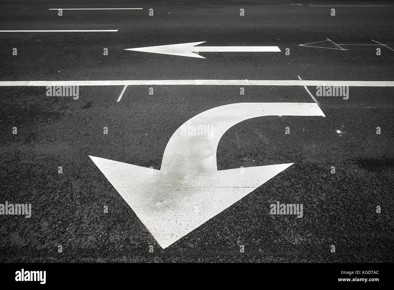 Turn or go straight street signs on asphalt, arrow pointing at viewer, conceptual background with focus on the first arrow. Stock Photo