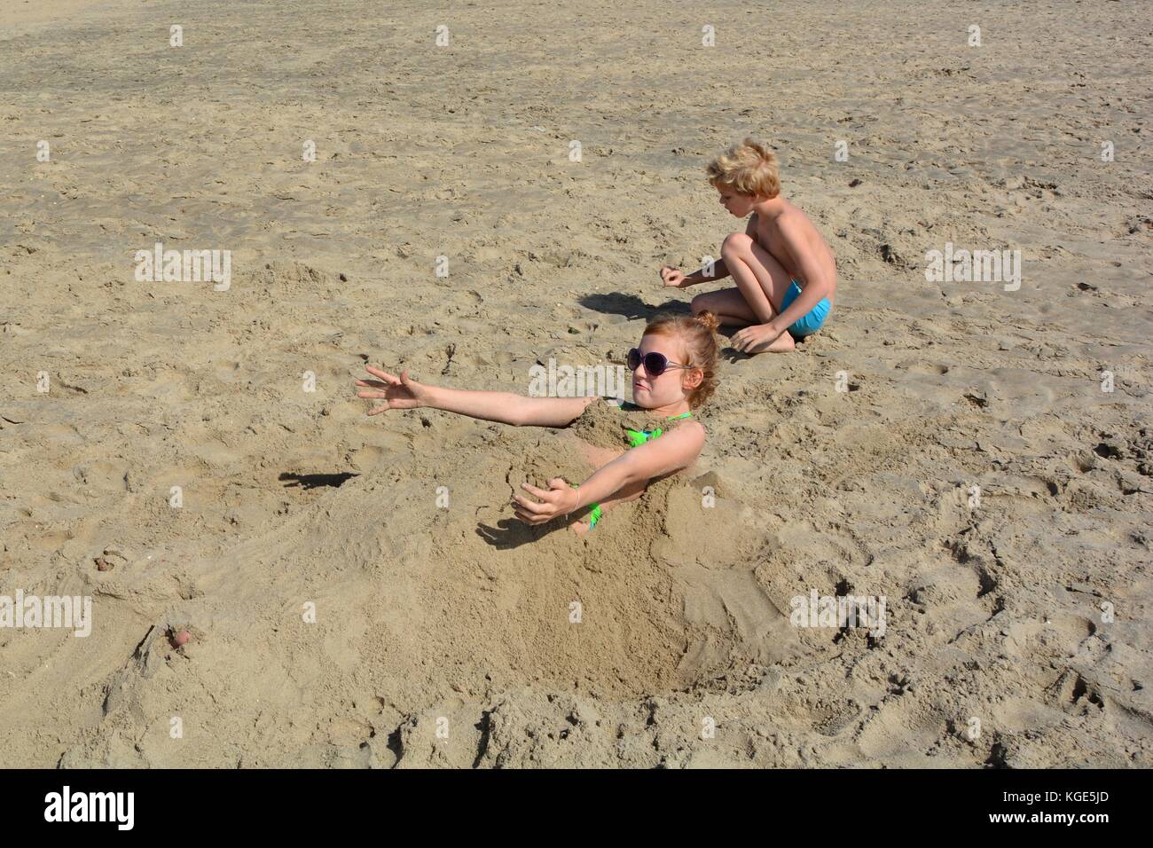 To get up in sand dug girl tried, boy sits besides Stock Photo