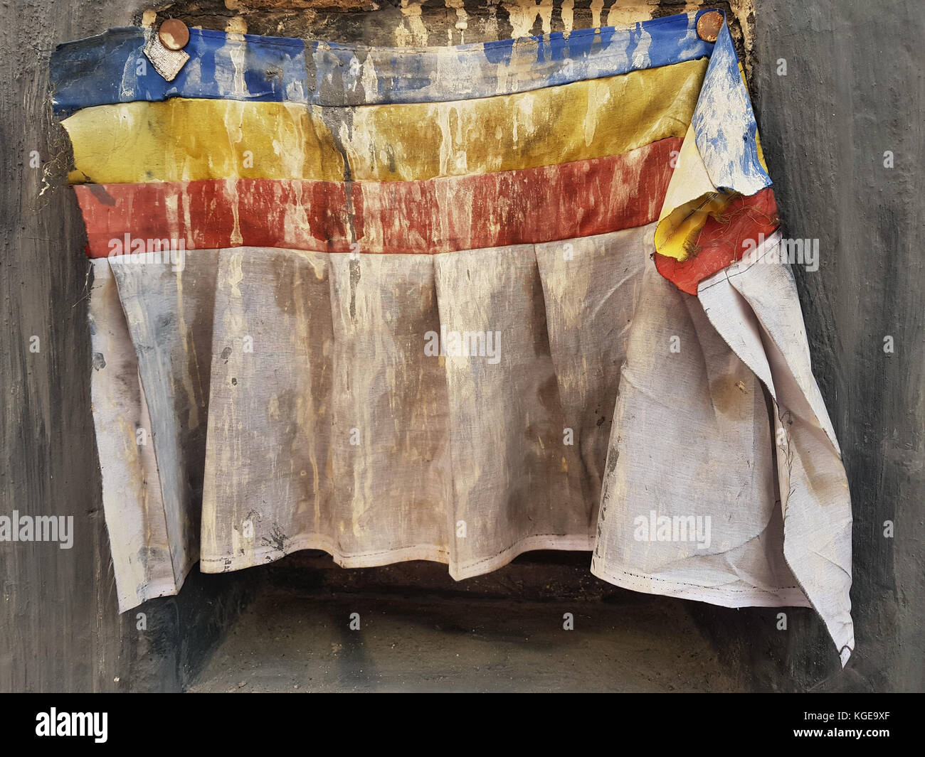 An old Buddhist monastery curtains dirty white with blue, yellow and red stripes hanging on a stone wall. Stock Photo