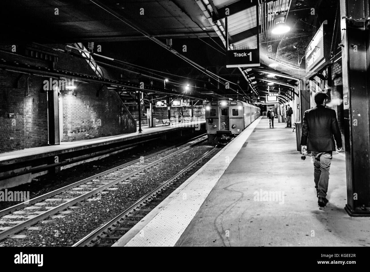 Summit, NJ USA - November 1, 2017:  A hip and fashionable man in hat and sport coat exists NJ Transit train station at night, black and white Stock Photo