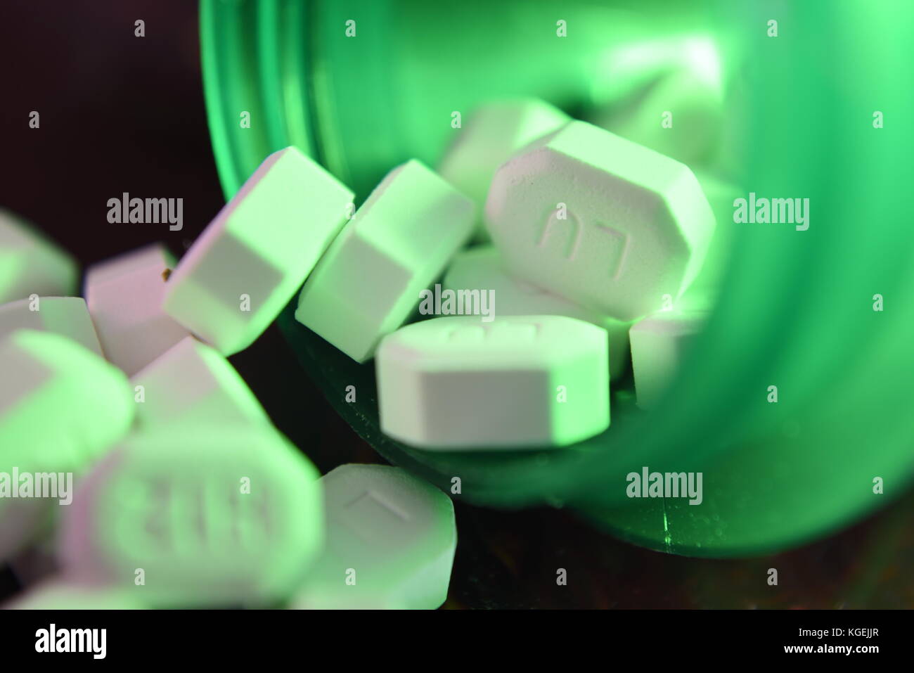 Macro and closeup shot of white pills spilling from green bottle Stock Photo