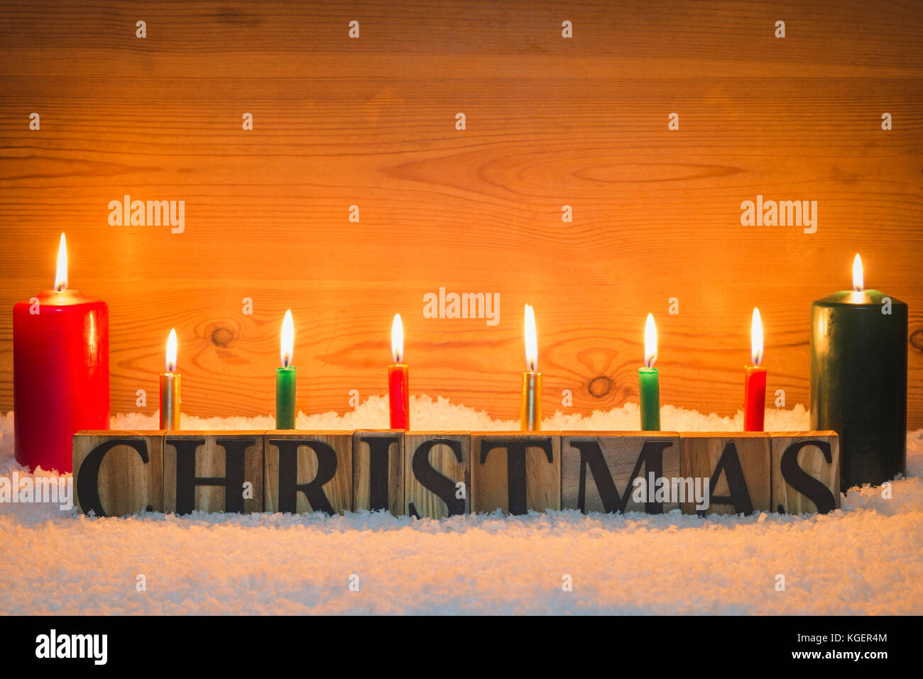 The word Christmas made from wooden letters in artificial snow with candles burning and a wooden background. Stock Photo