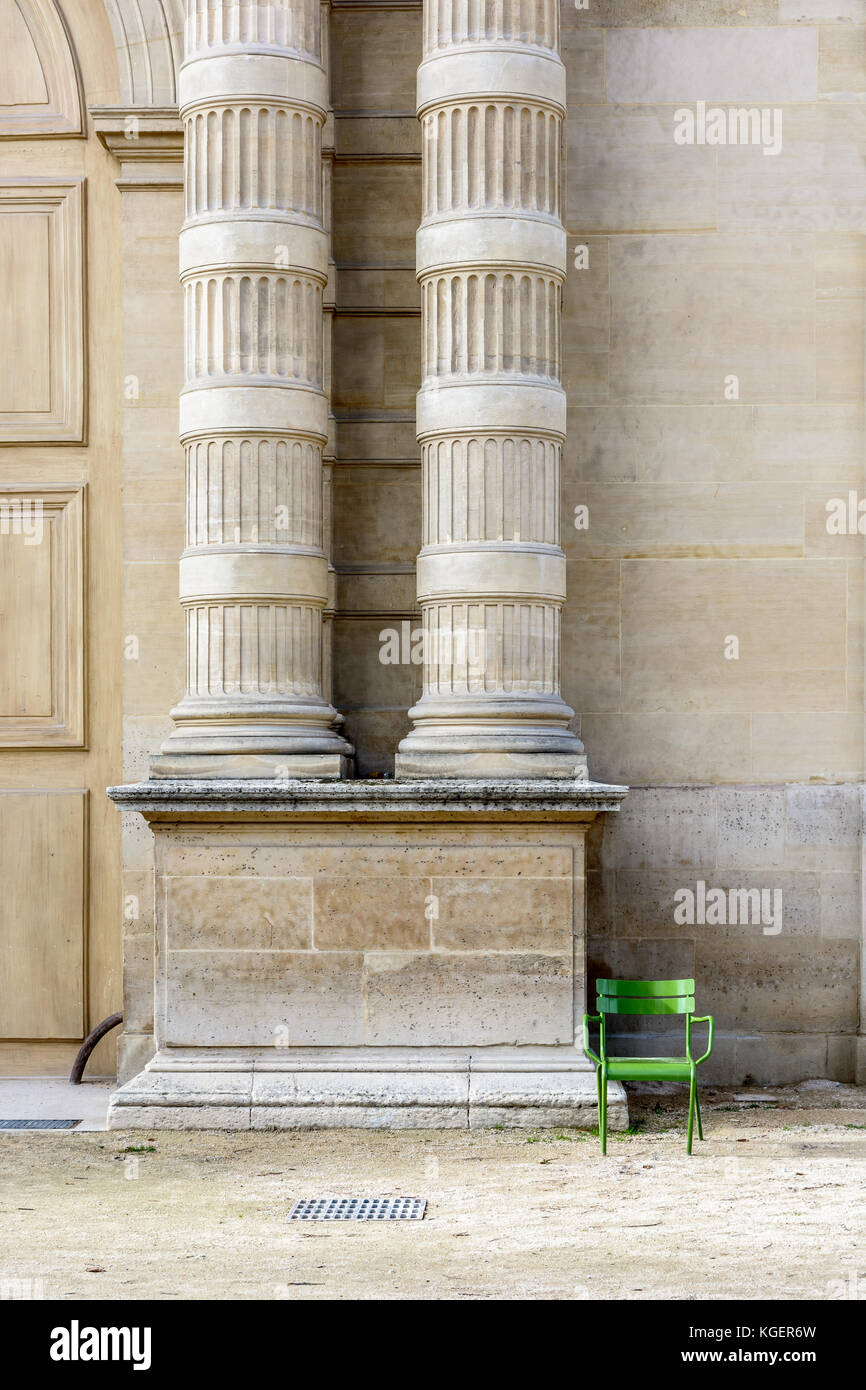 A green metal lawn chair, typical of the parisian public gardens, alone beside two fluted stone columns. Stock Photo