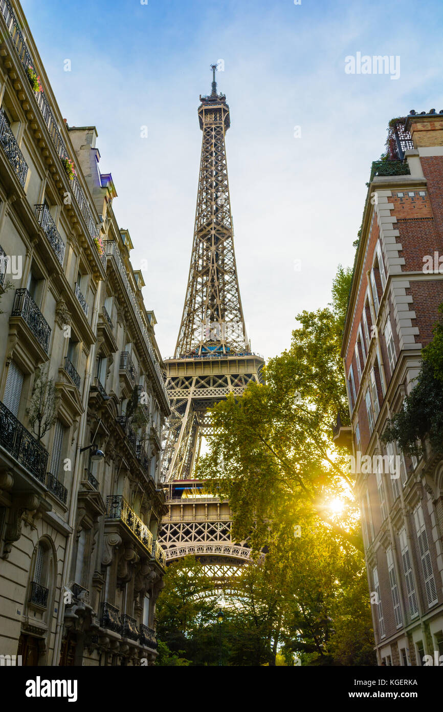 View of the majestic Eiffel Tower in its immediate neighborhood with typical parisian buildings in the foreground and the setting sun bursting through Stock Photo