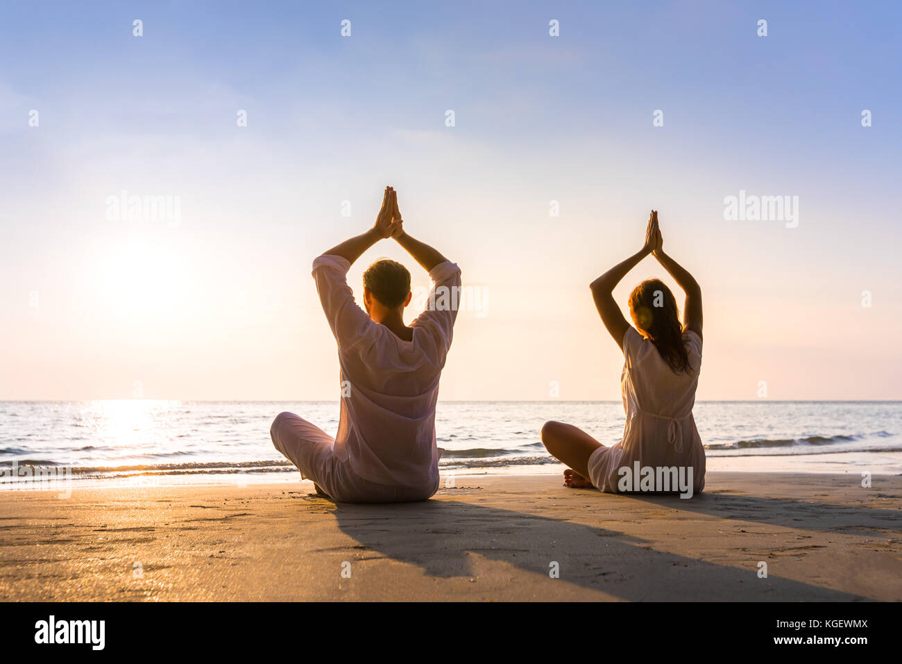 Couple practicing yoga on the beach in morning sunlight, relaxation, balance and harmony, healthy lifestyle Stock Photo
