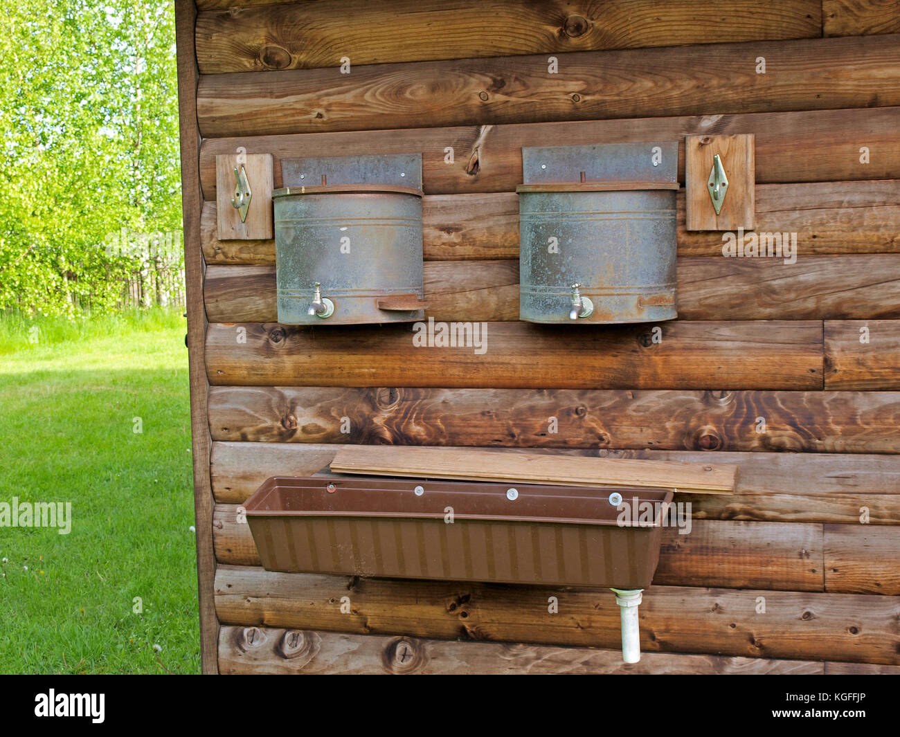 Sink and water tanks with taps on log house wall for washing outdoor