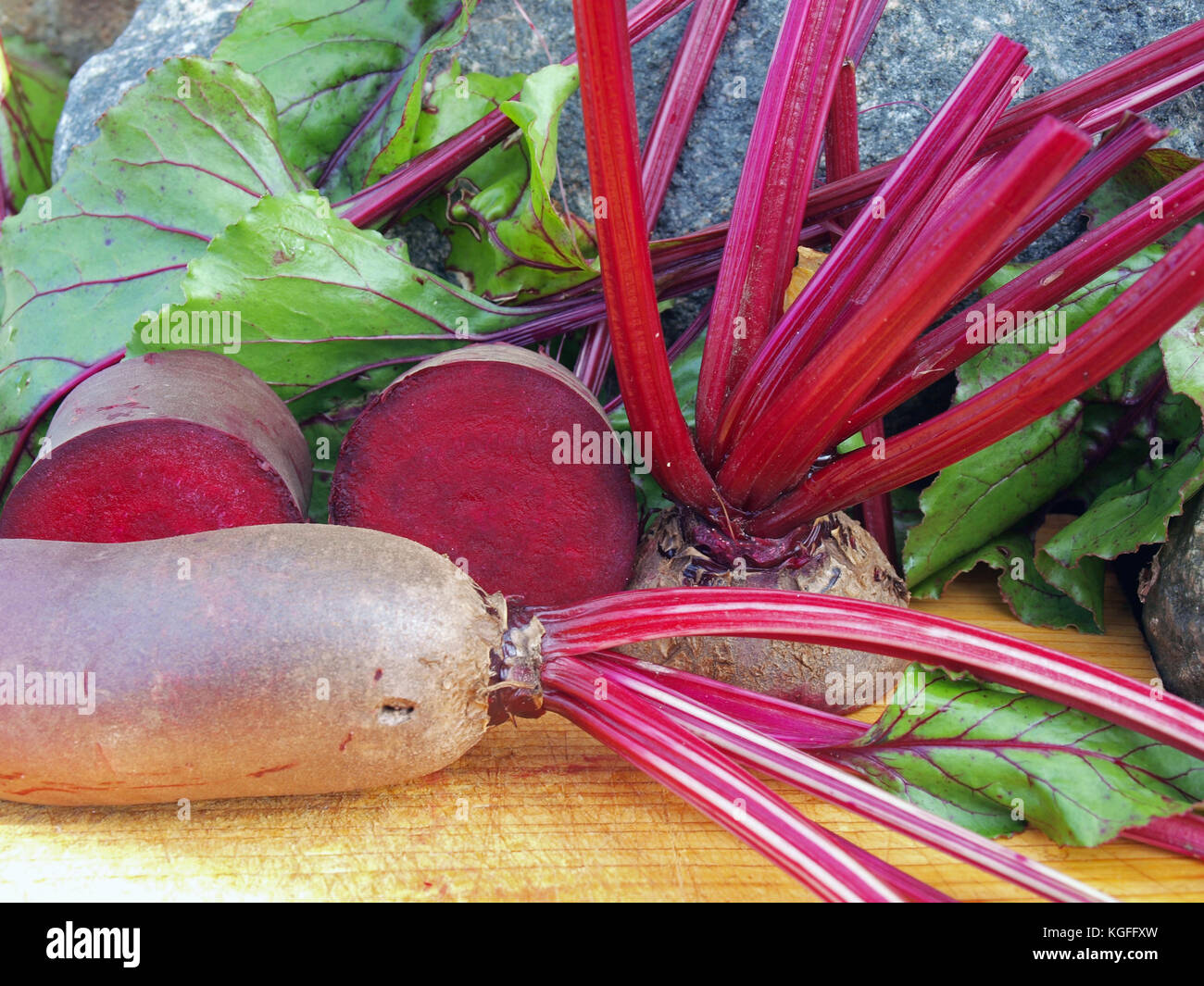 Bisected red beets and leaves on wooden board close up. Stock Photo