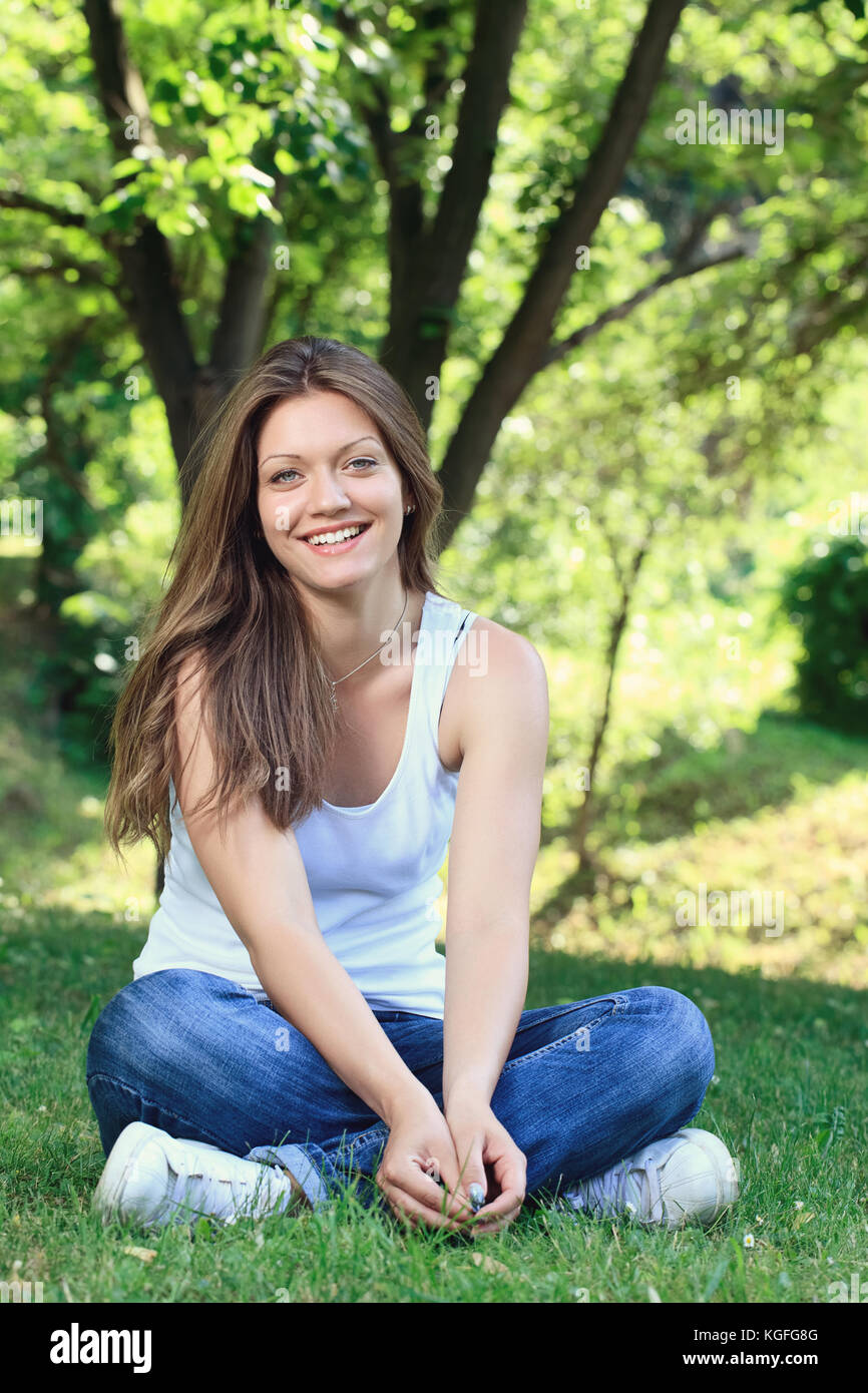 Young girl siting on grass in park and smiling Stock Photo - Alamy