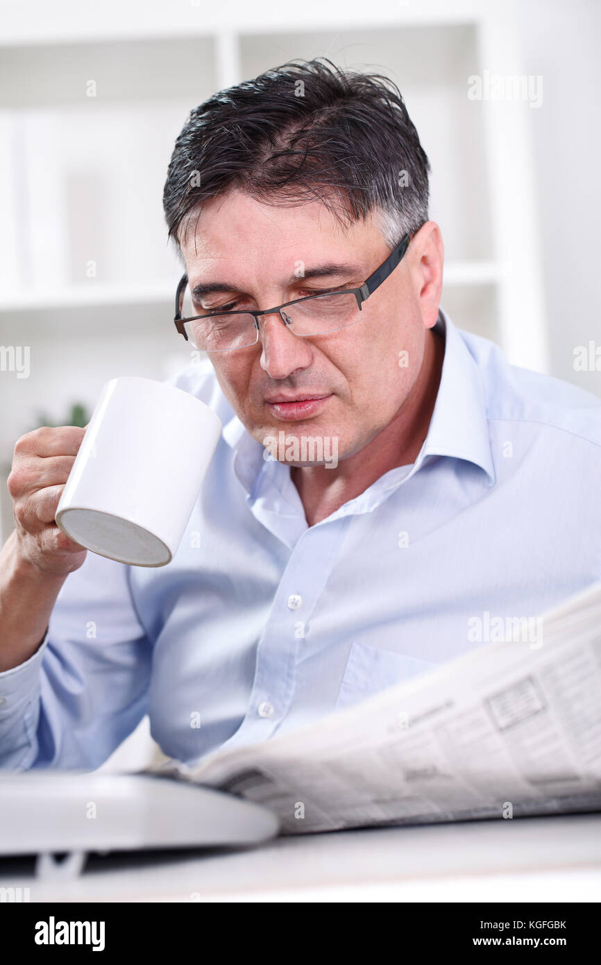 Senior businessman on coffee break in office lobby, reading papers