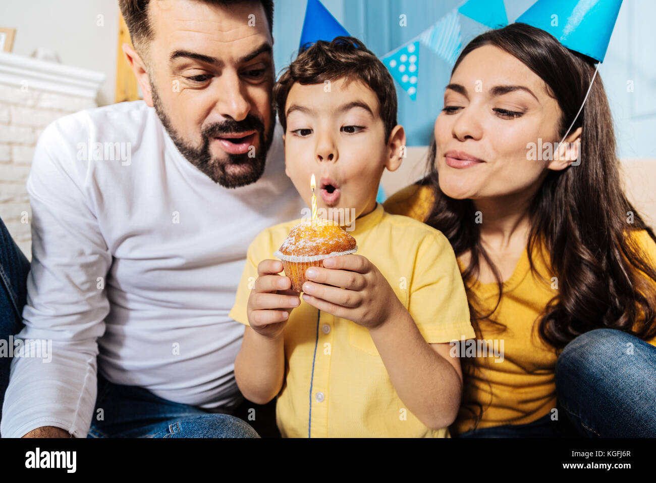 Happy family blowing out candle on birthday muffin together Stock Photo