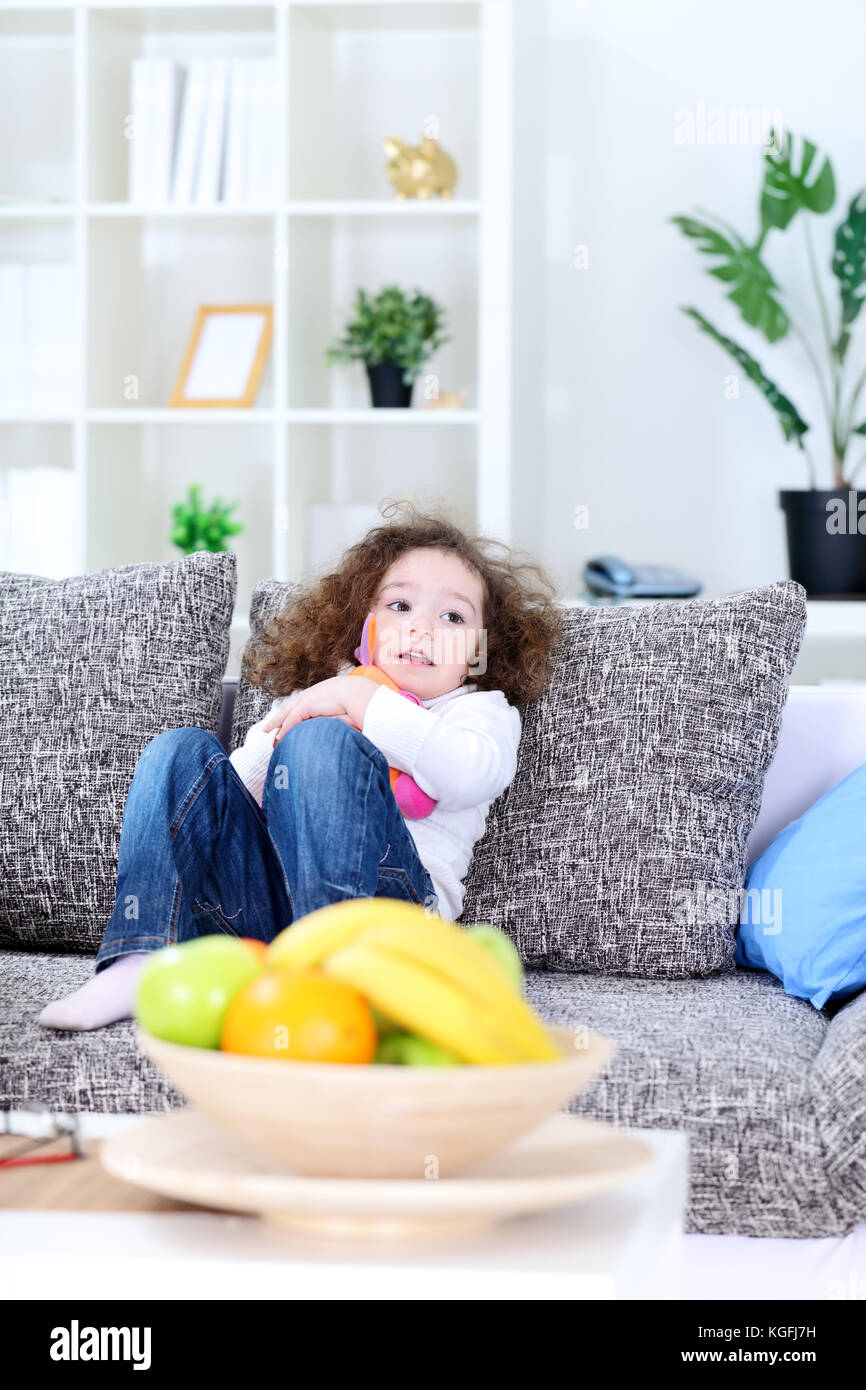 Little girl sitting on sofa in living room and hugging her soft toy ...