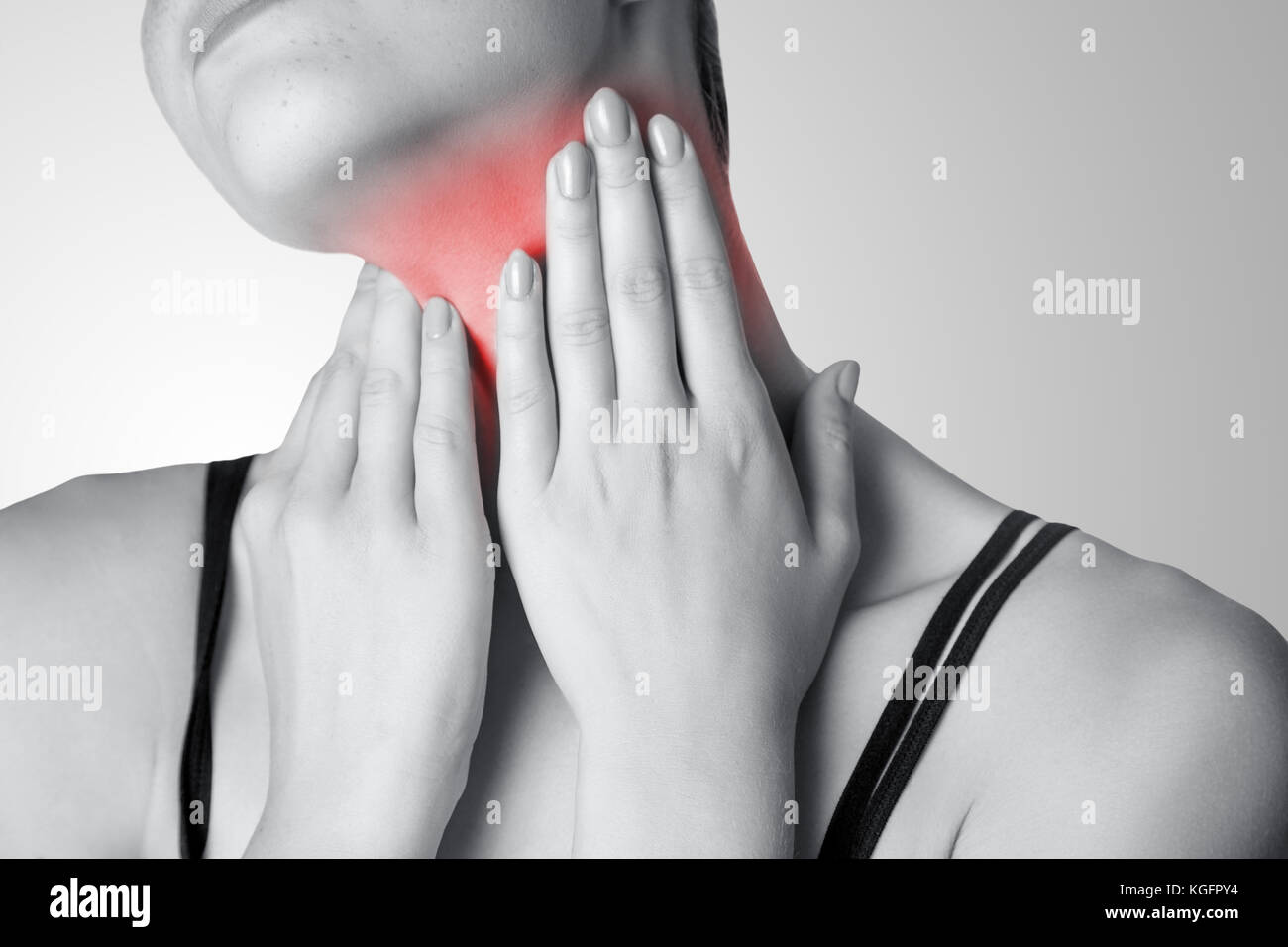 Closeup view of a young woman with pain on neck or thyroid gland on gray background. Black and white photo with red dot. Stock Photo