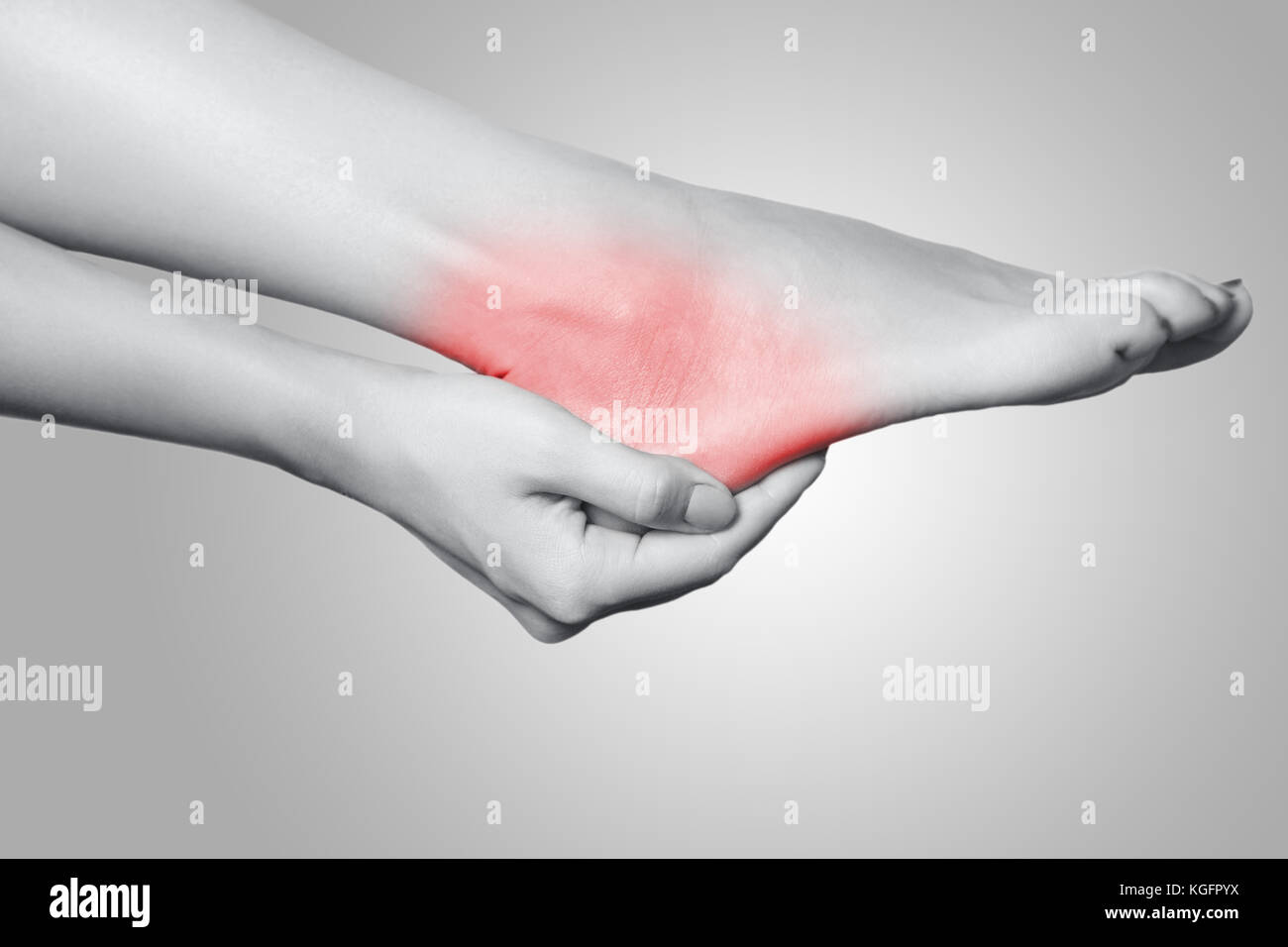 Closeup view of a young woman with pain on leg on gray background. Black and white photo with red dot. Stock Photo