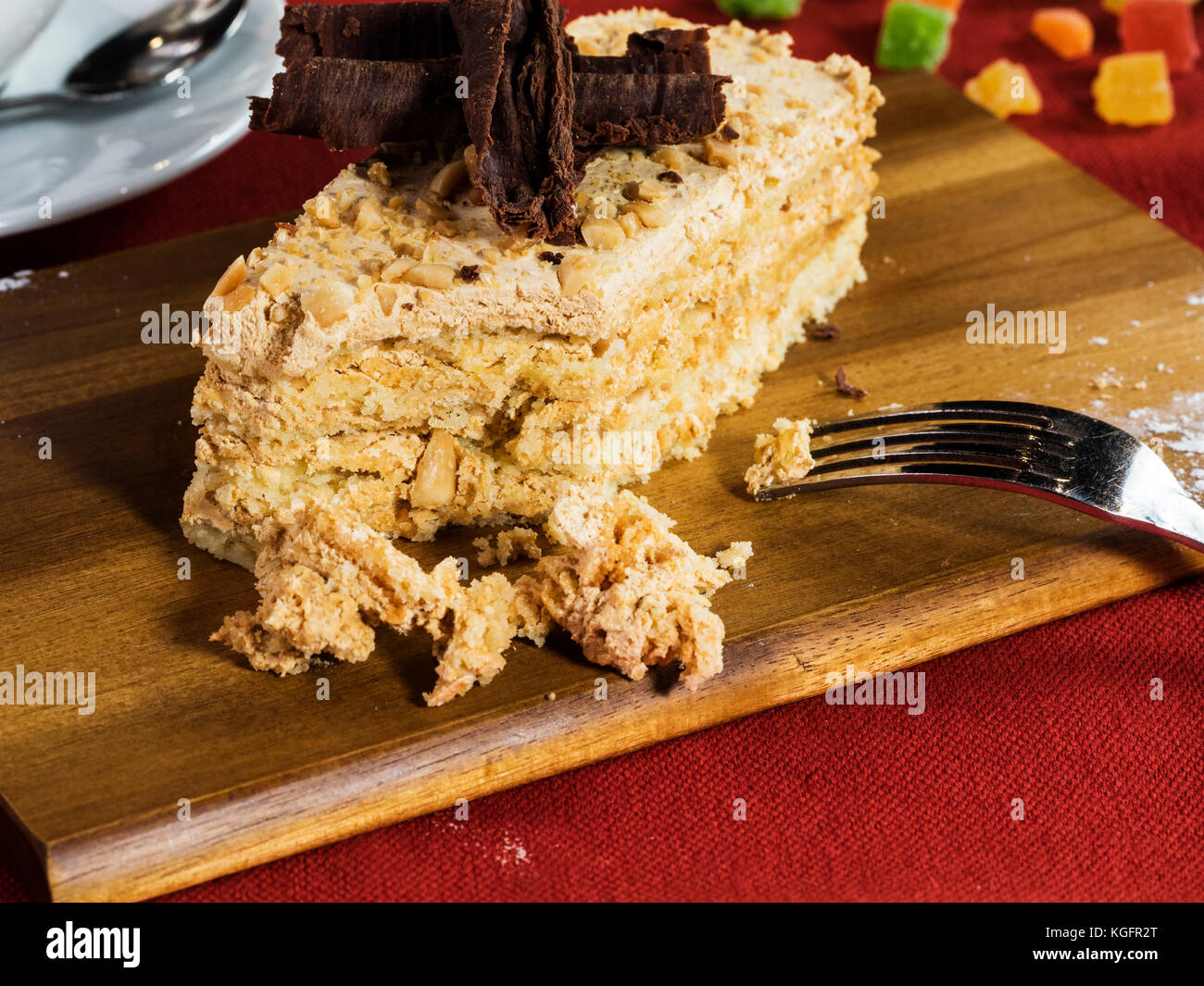 piece of shortcake cake in walnuts, decorated with crumbs and chocolate on a wooden cutting board on a red tablecloth with a cup of tea and candied fr Stock Photo