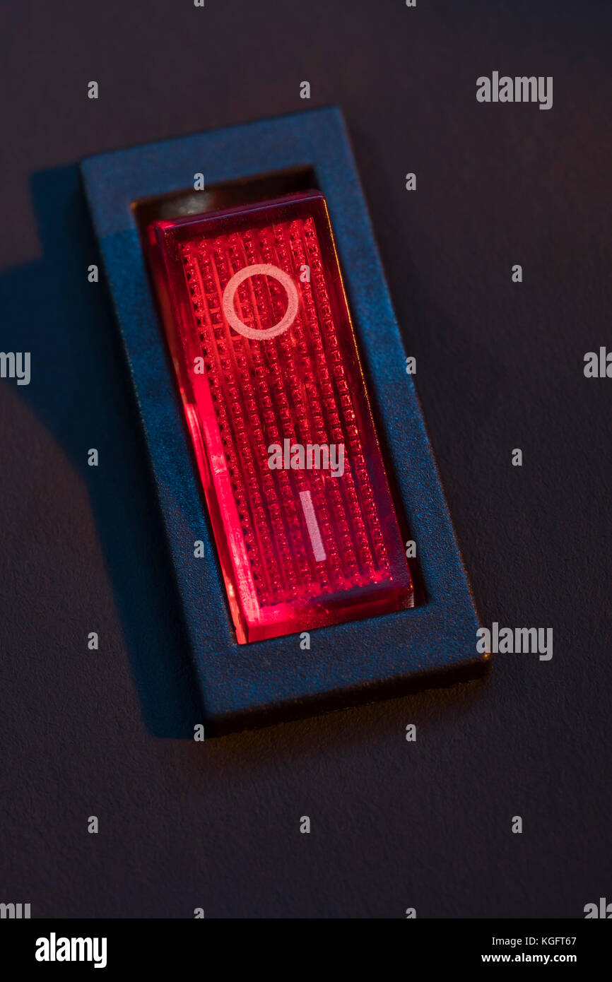 Illuminated red electrical switch on black background potential