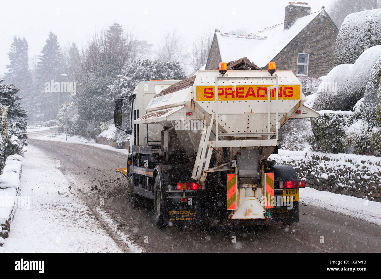 Cold, snowy winter scene as gritter lorry with snow plough, drives, spreading grit & clearing deserted road - Hawksworth, West Yorkshire, England, UK. Stock Photo