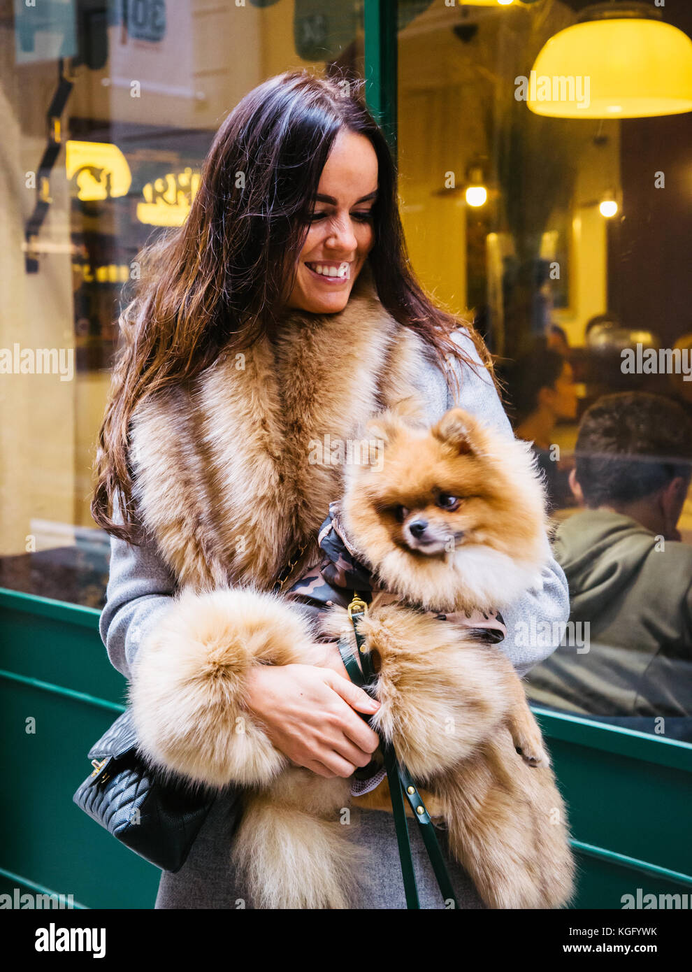 Portrait of woman smiling in fur coat, holding Pomeranian dog Stock Photo