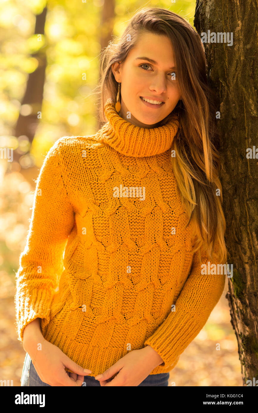 Beautiful young woman smiling in autumn park and standing near tree in ...