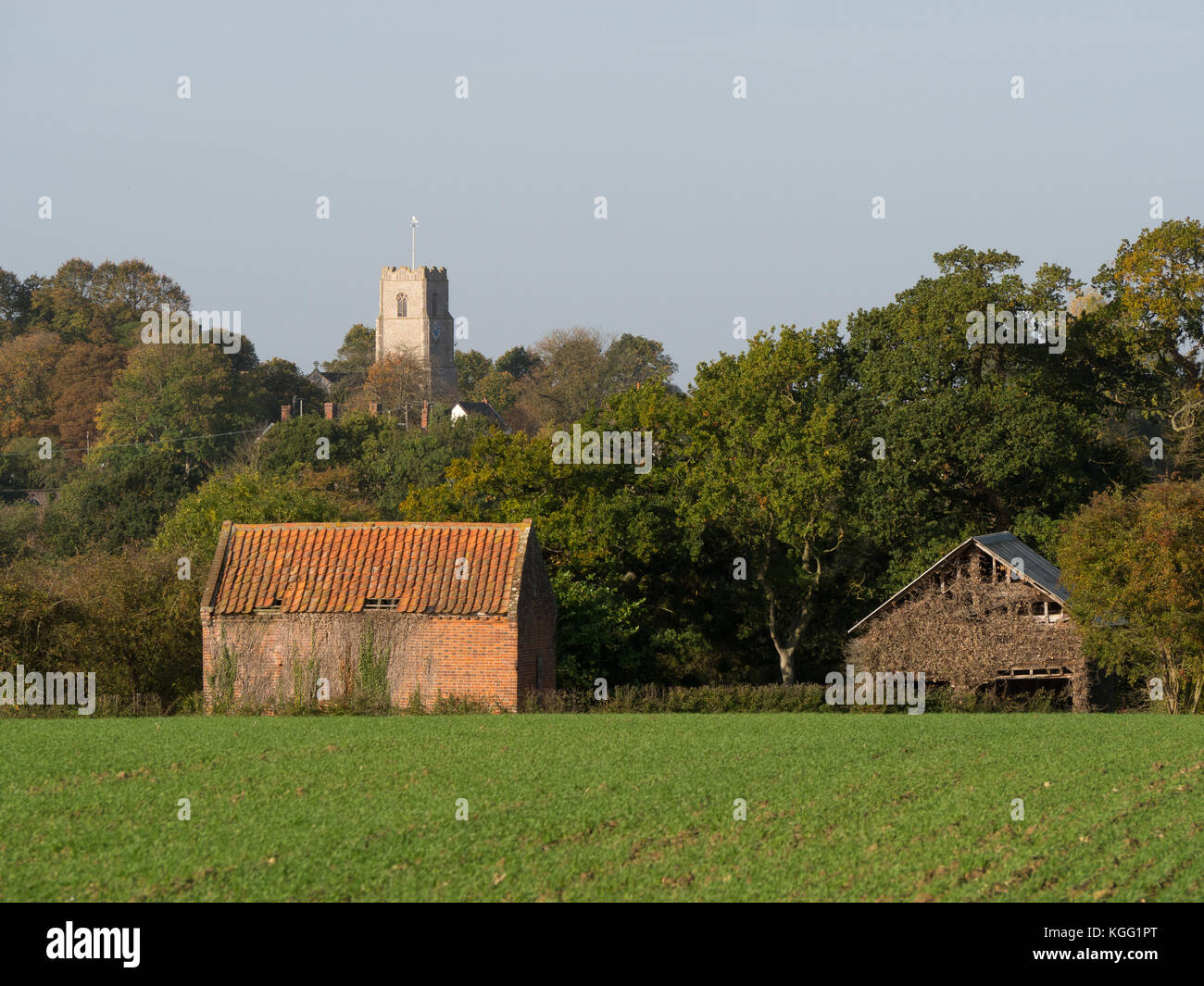 Traditional English rural landscape with brick farm building and church visible in the background Stock Photo