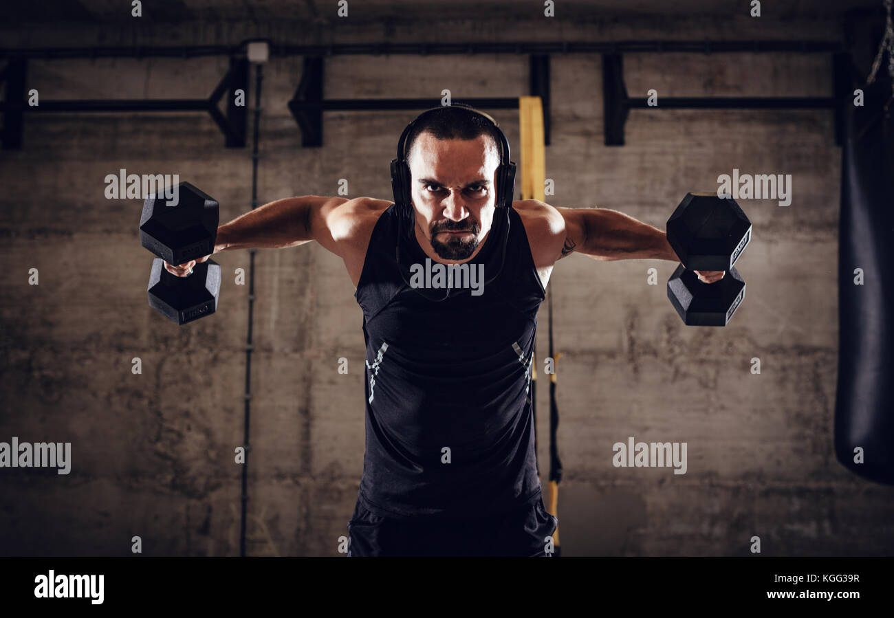 Young muscular man doing hard exercise with dumbbells for shoulders on