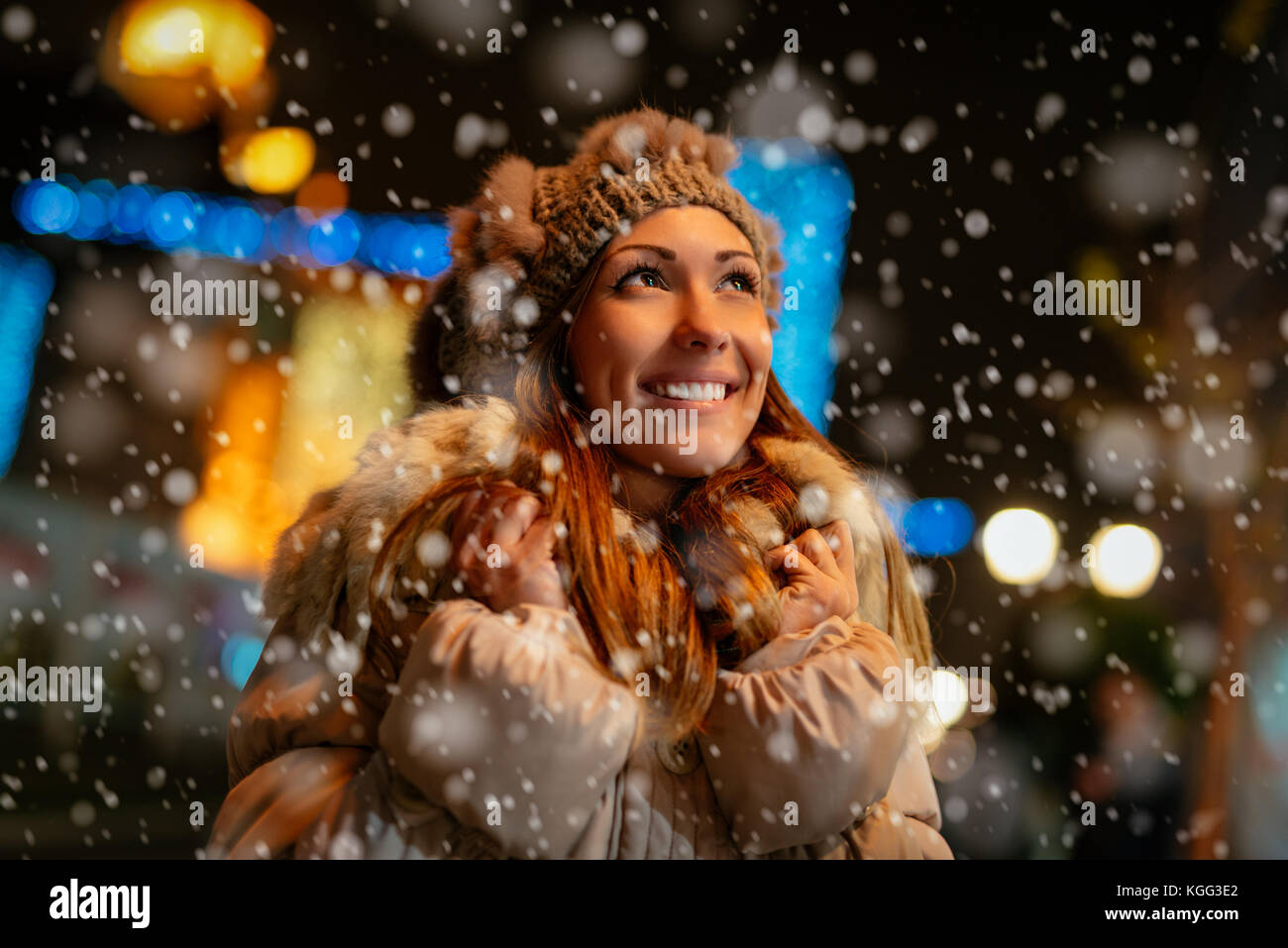 Smiling beautiful young woman in warm clothing enjoying while snowing in winter holiday time. Stock Photo