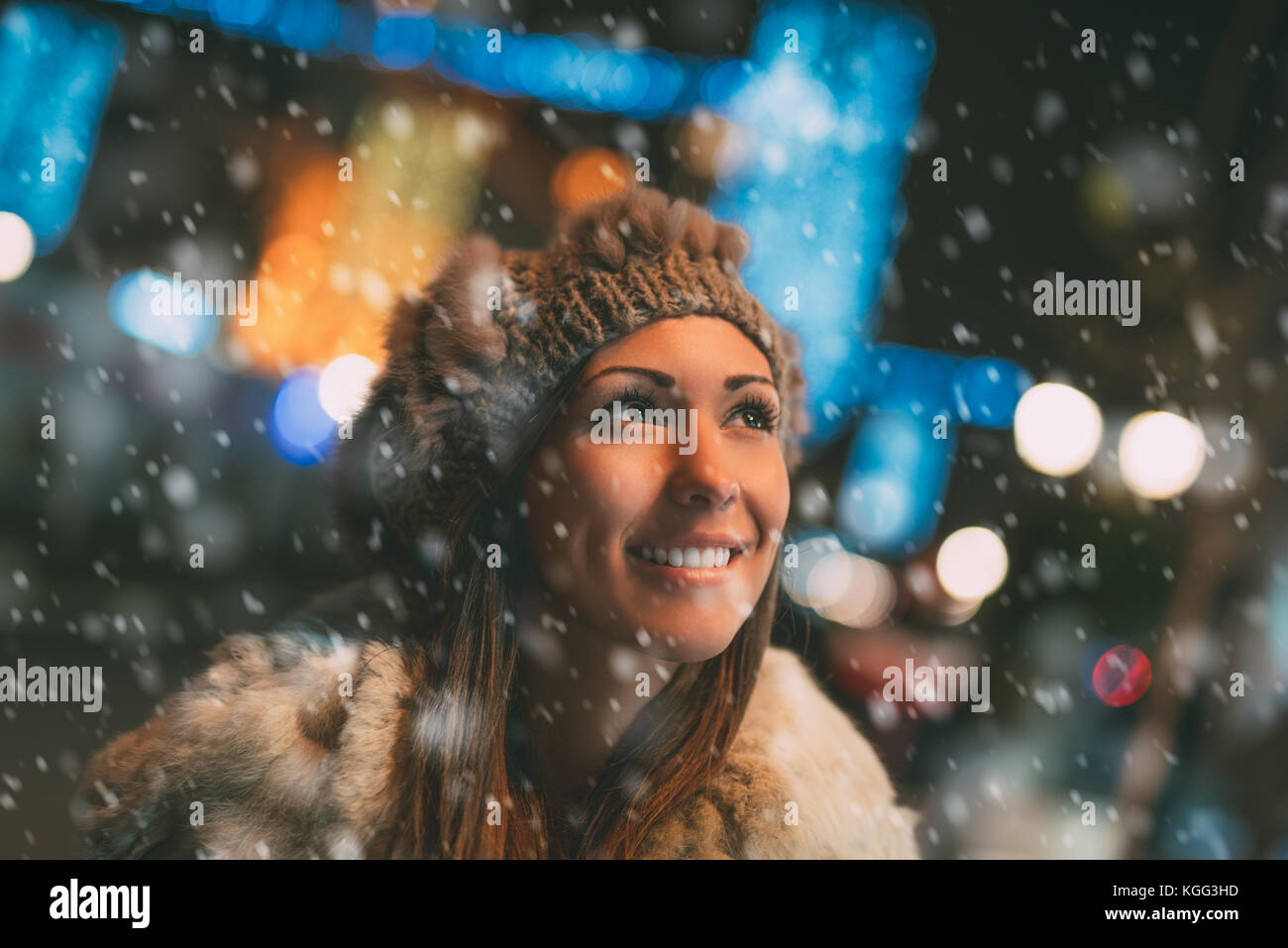 Smiling beautiful young woman in warm clothing enjoying while snowing in winter holiday time. Stock Photo