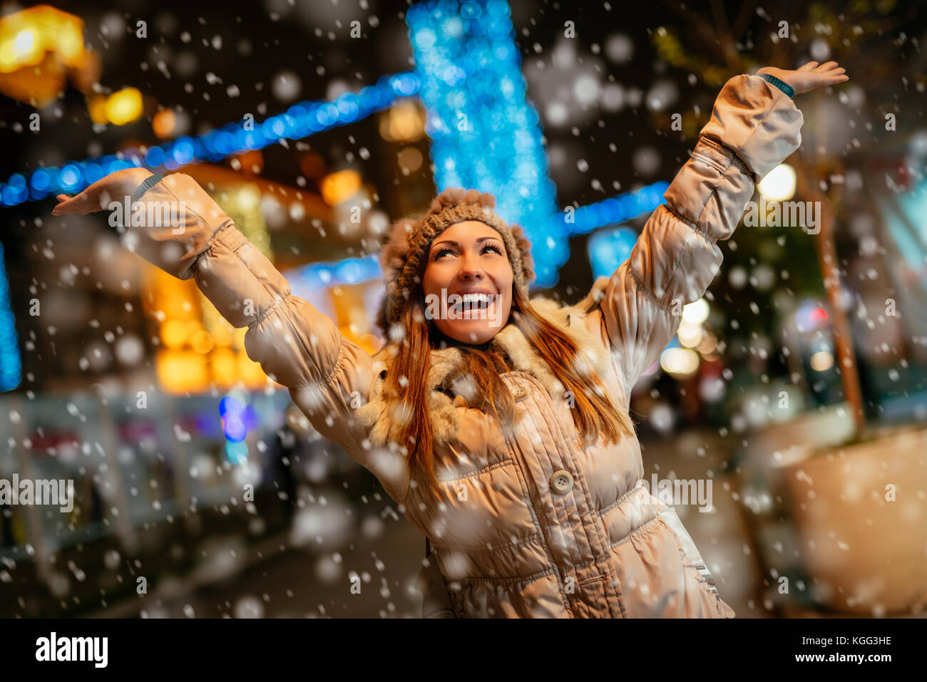 Cheerful beautiful young woman in warm clothing having fun while snowing in winter holiday time. Stock Photo